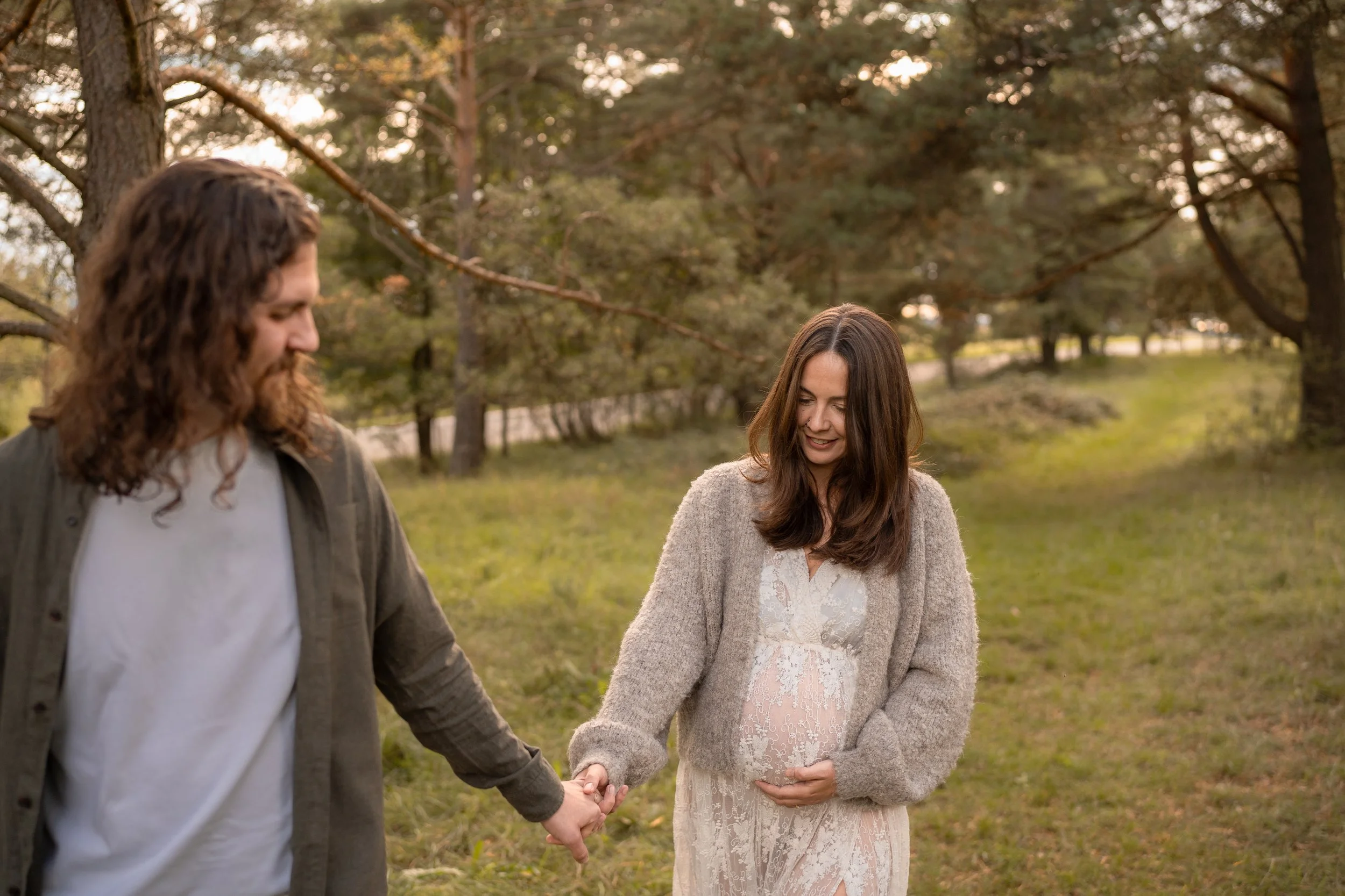 Ein Paar hält sich bei Sonnenuntergang in einem Park, die Frau zeigt auf ihren gebäbten Bauch, sie freut sich auf ein Kind.