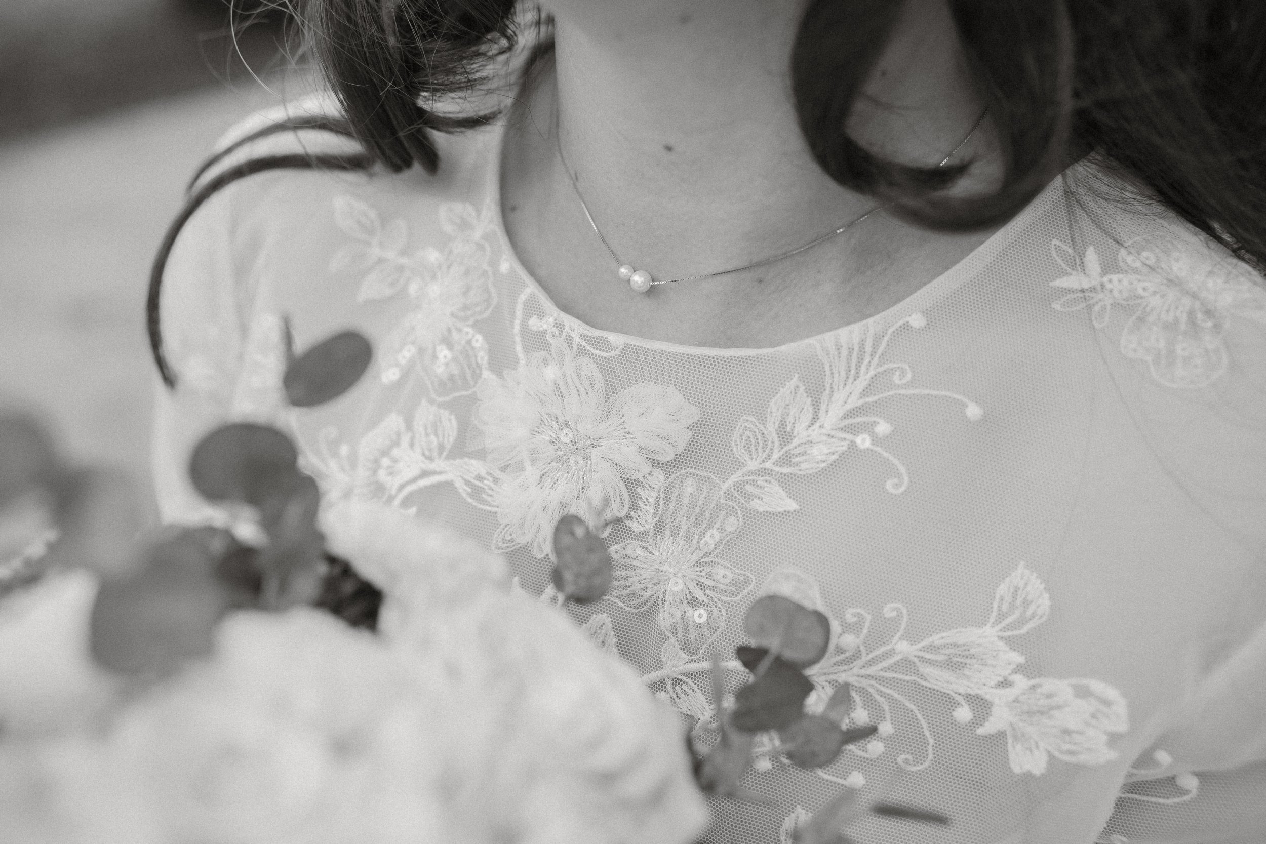 Nahaufnahme einer Frau in einem schwarzen und weißen Kleid mit floralem Muster, die eine Perlenkette trägt. Der Fokus liegt auf dem oberen Brustbereich und der Kleidung, im Hintergrund unscharf.