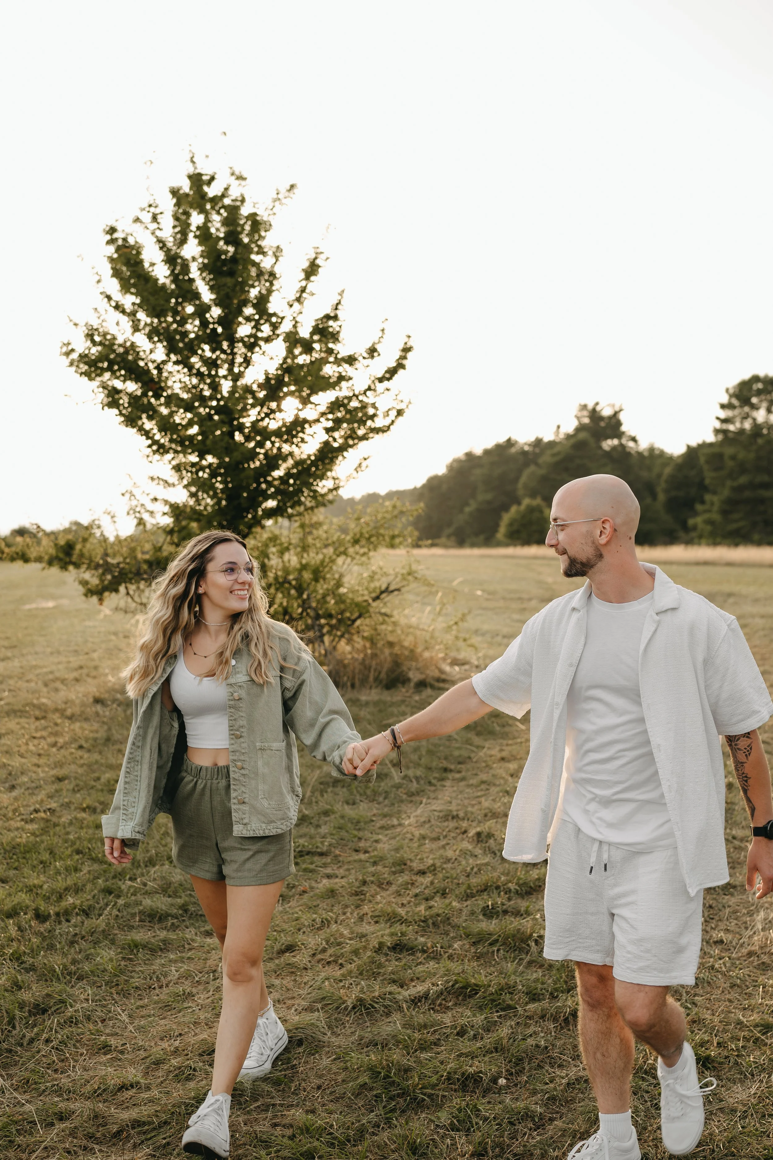 Ein junges Paar läuft lachend über eine Wiese, hält Händchen und genießt die Natur bei Sonnenuntergang.