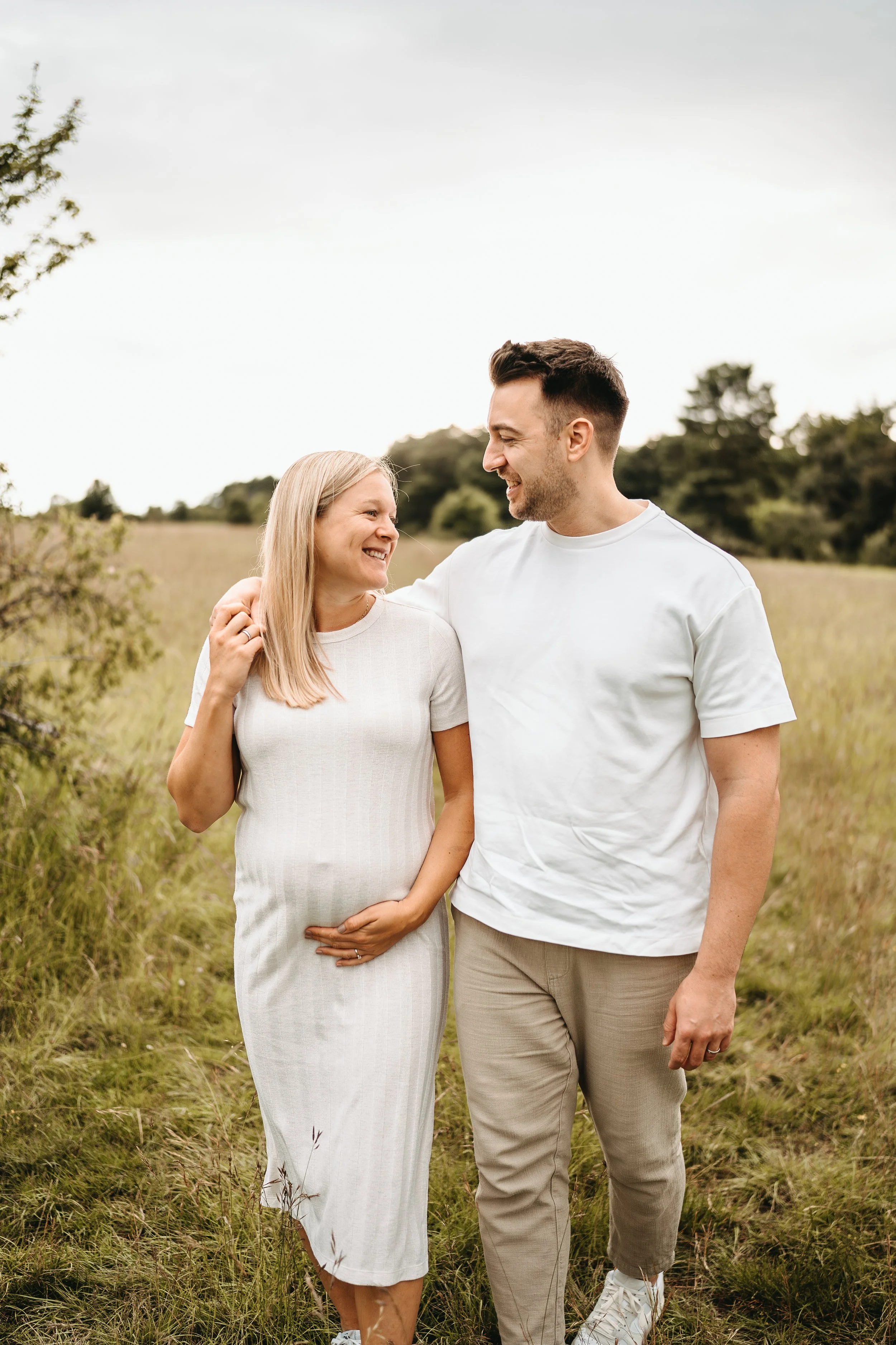 Ein glückliches Paar, eine schwangere Frau und ein Mann, gehen im Freien durch ein Grasfeld. Sie lächeln sich an und scheinen Freude und Zuneigung zu zeigen.