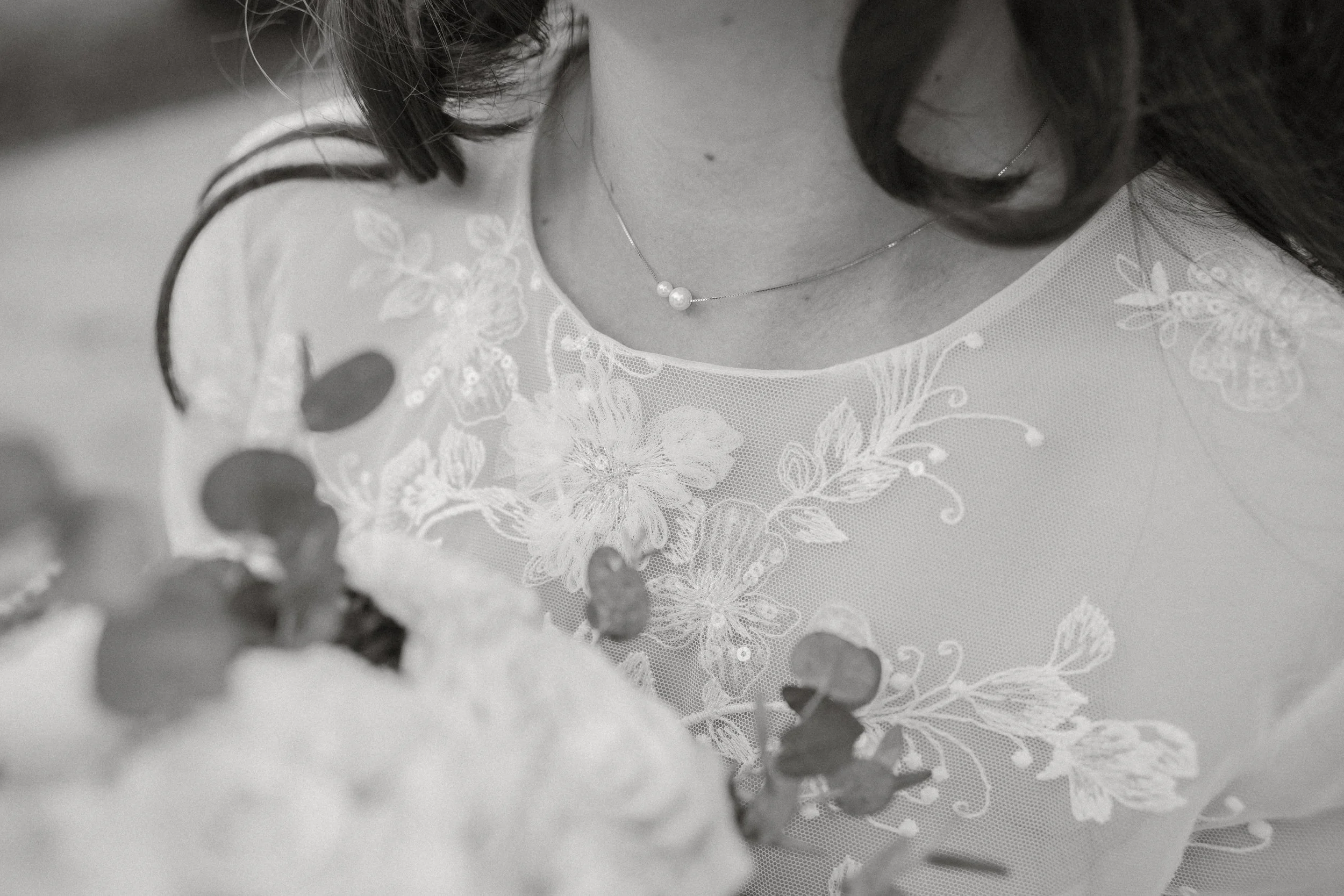 Nahaufnahme eines Brautkleides mit stickierten Blumenmustern und einer Perlenkette.