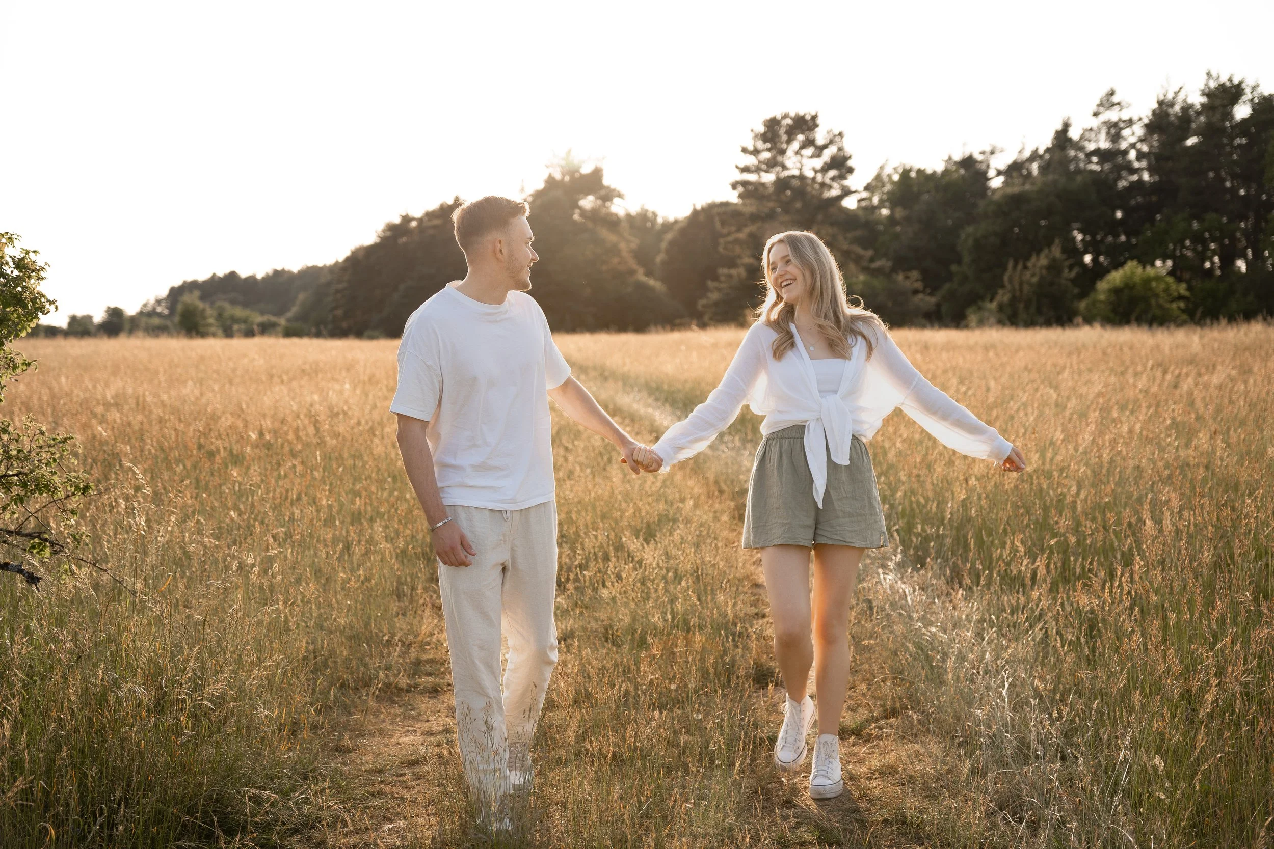 Ein lachendes Paar läuft Hand in Hand durch ein Getreidefeld bei Sonnenuntergang.