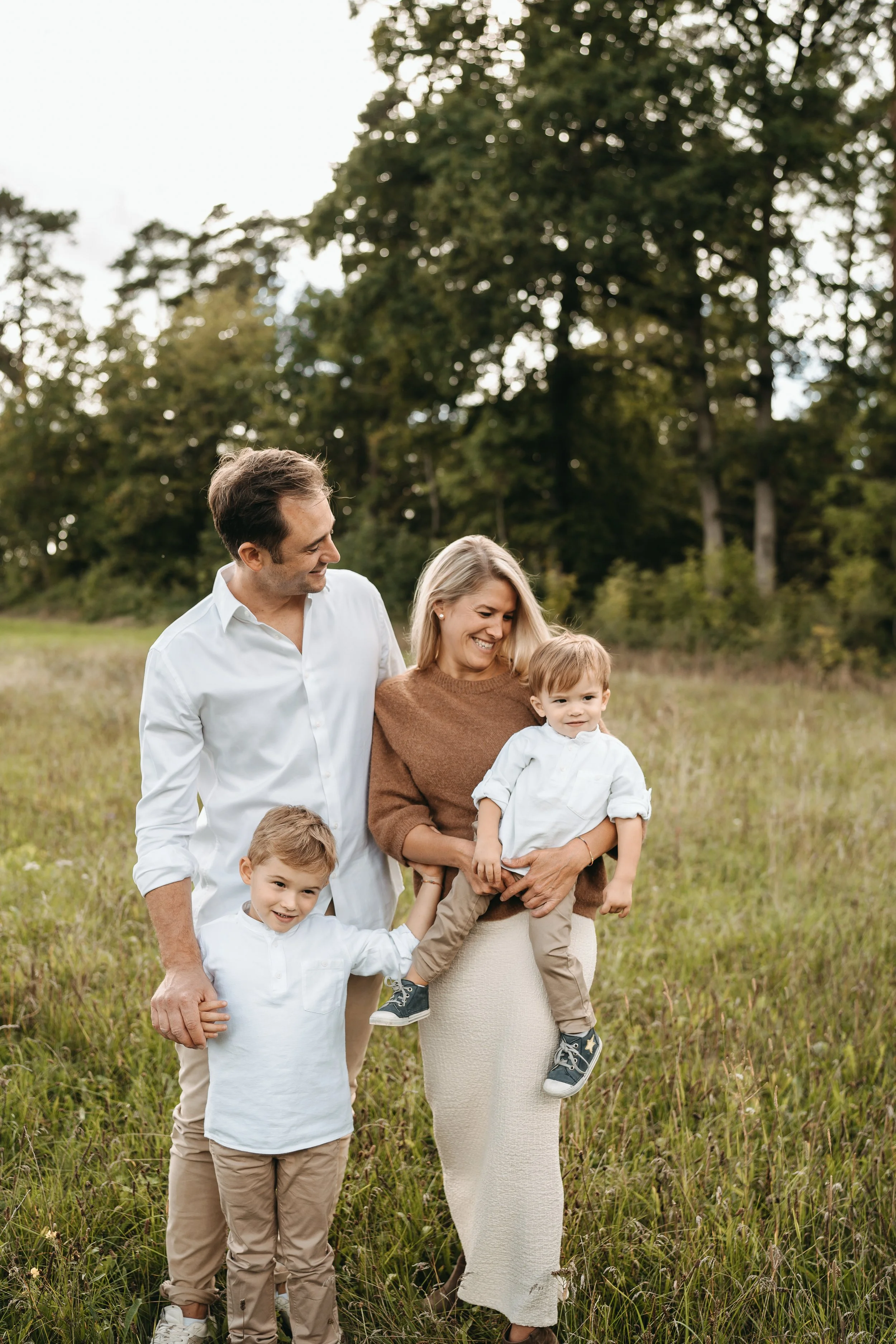 Familie mit zwei kleinen Jungen und einer Frau, die im Freien in einem Grasefeld spazieren geht.