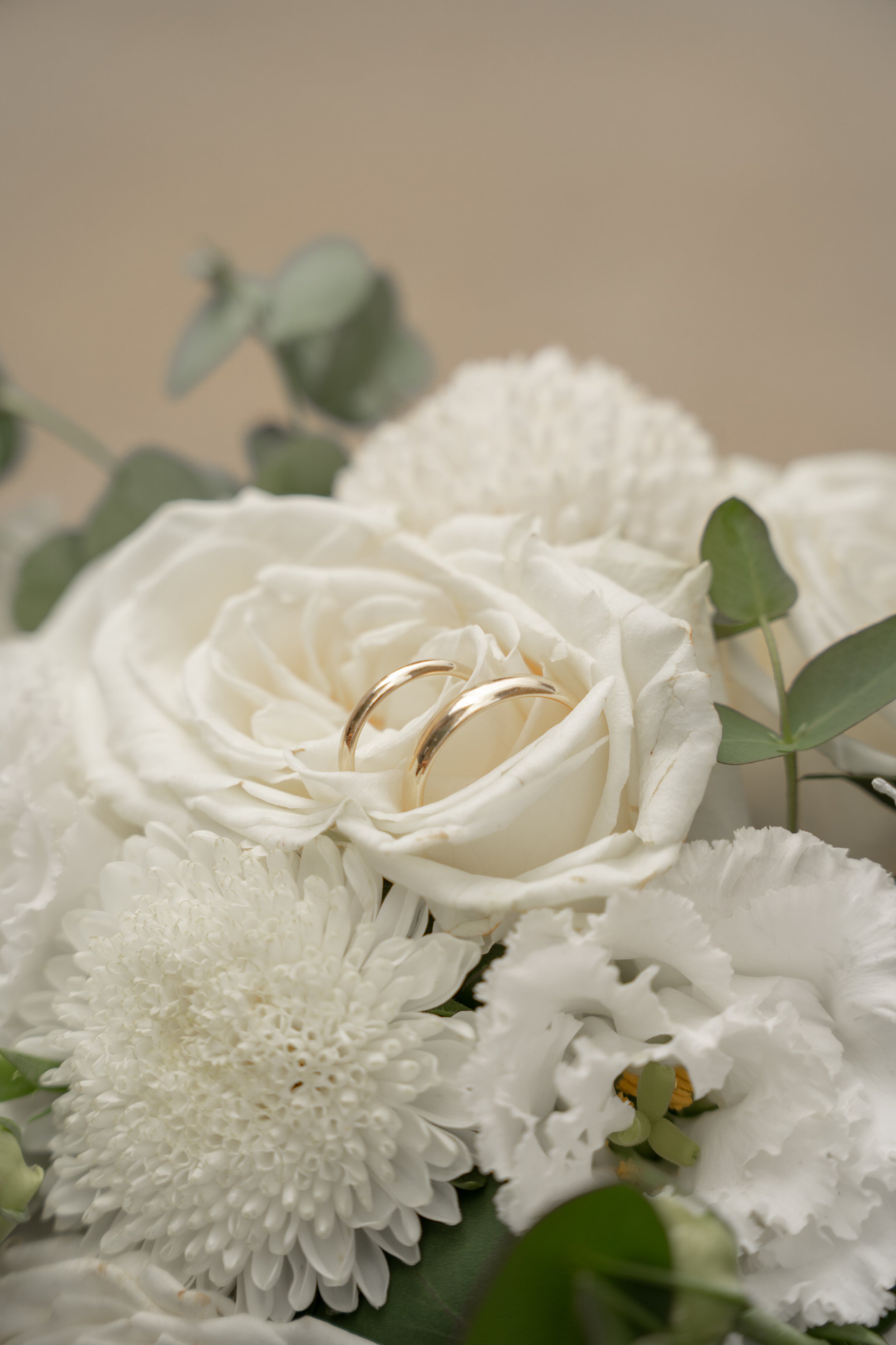 Zwei goldene Eheringe liegen auf weißen Blüten, darunter befinden sich grüne Blätter.