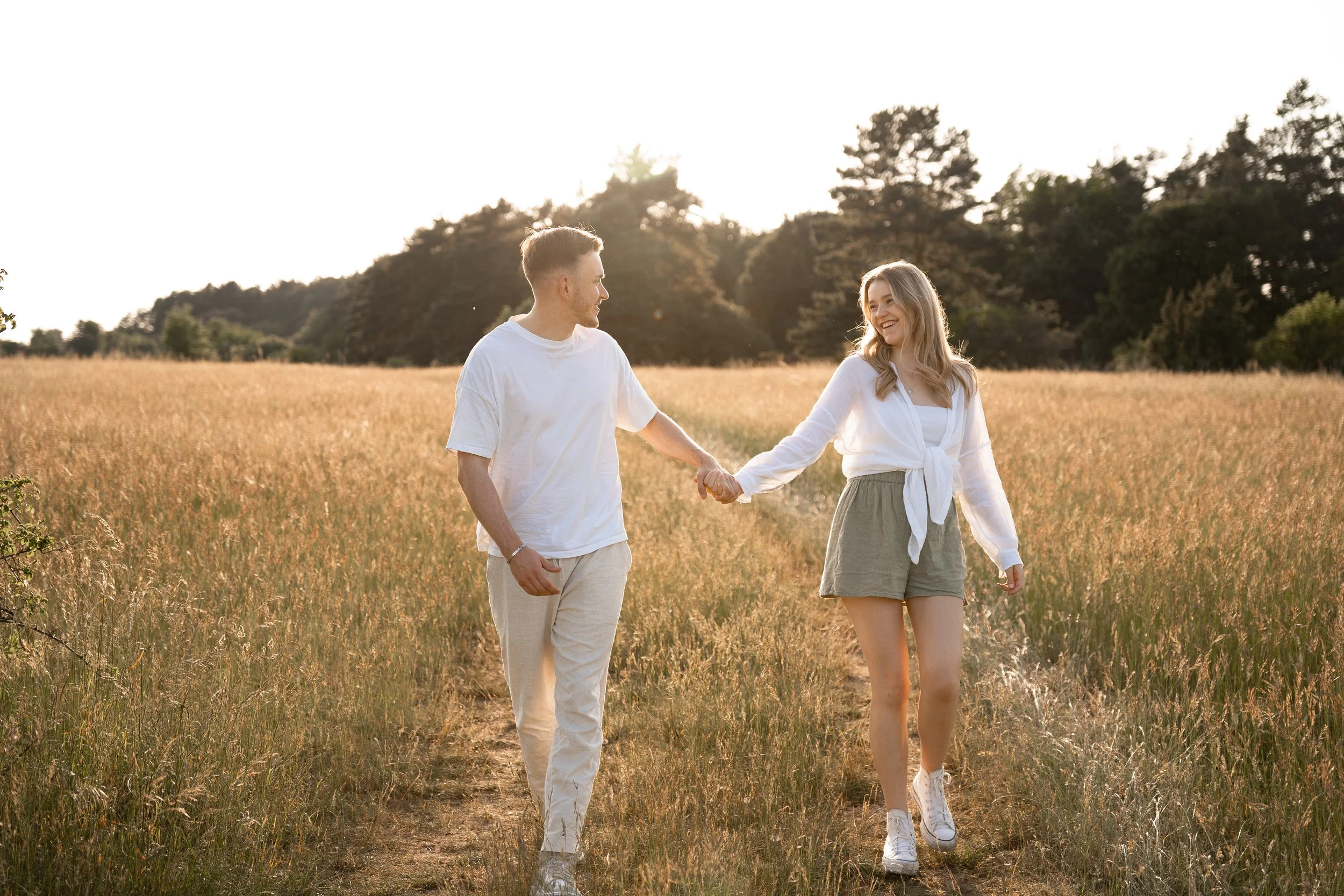 Ein Paar läuft Hand in Hand durch ein Feld bei Sonnenuntergang, lachend und glücklich.