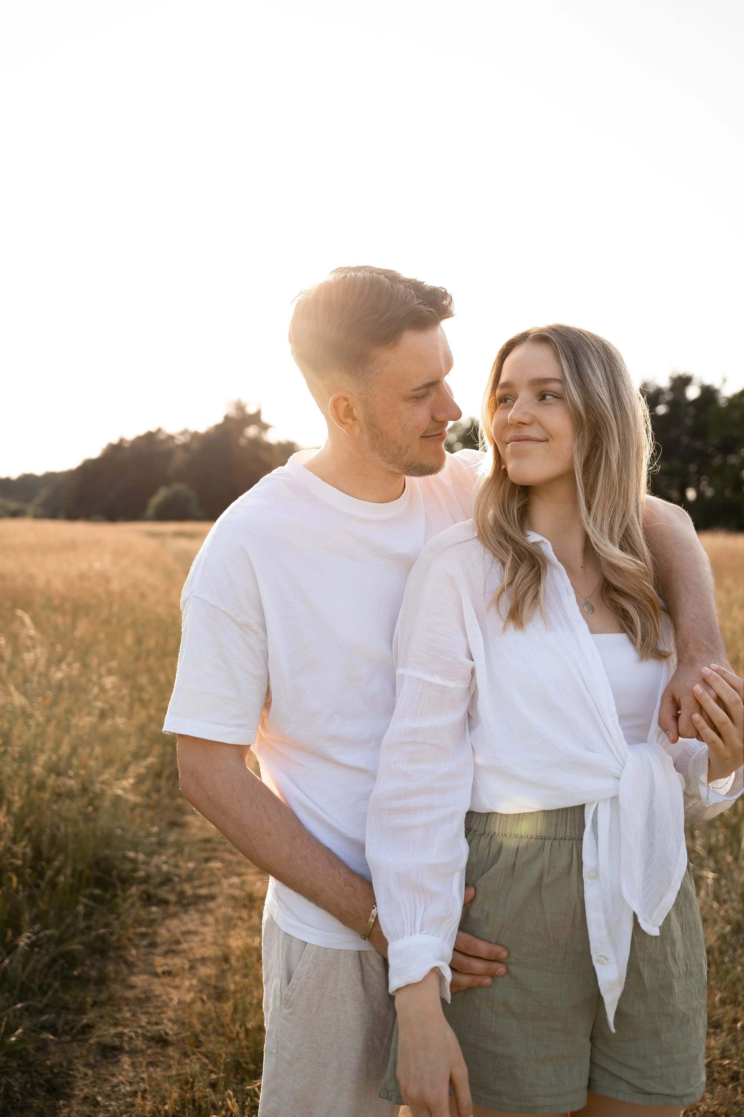 Ein junges Paar steht in einem Feld bei Sonnenuntergang und schaut sich an.