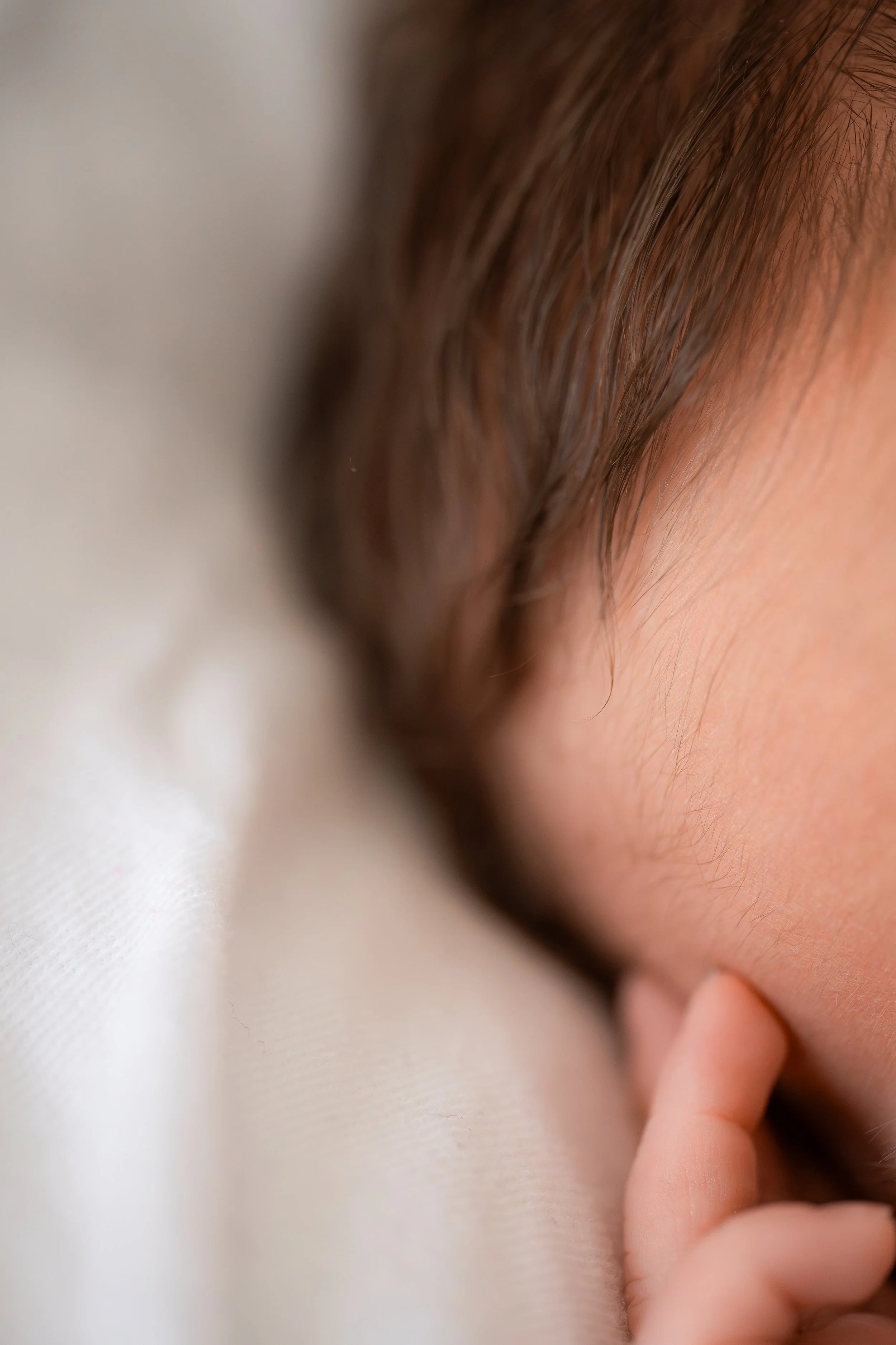 Nahaufnahme eines schlafenden Babys mit geschlossenem Auge und Finger an der Wange.