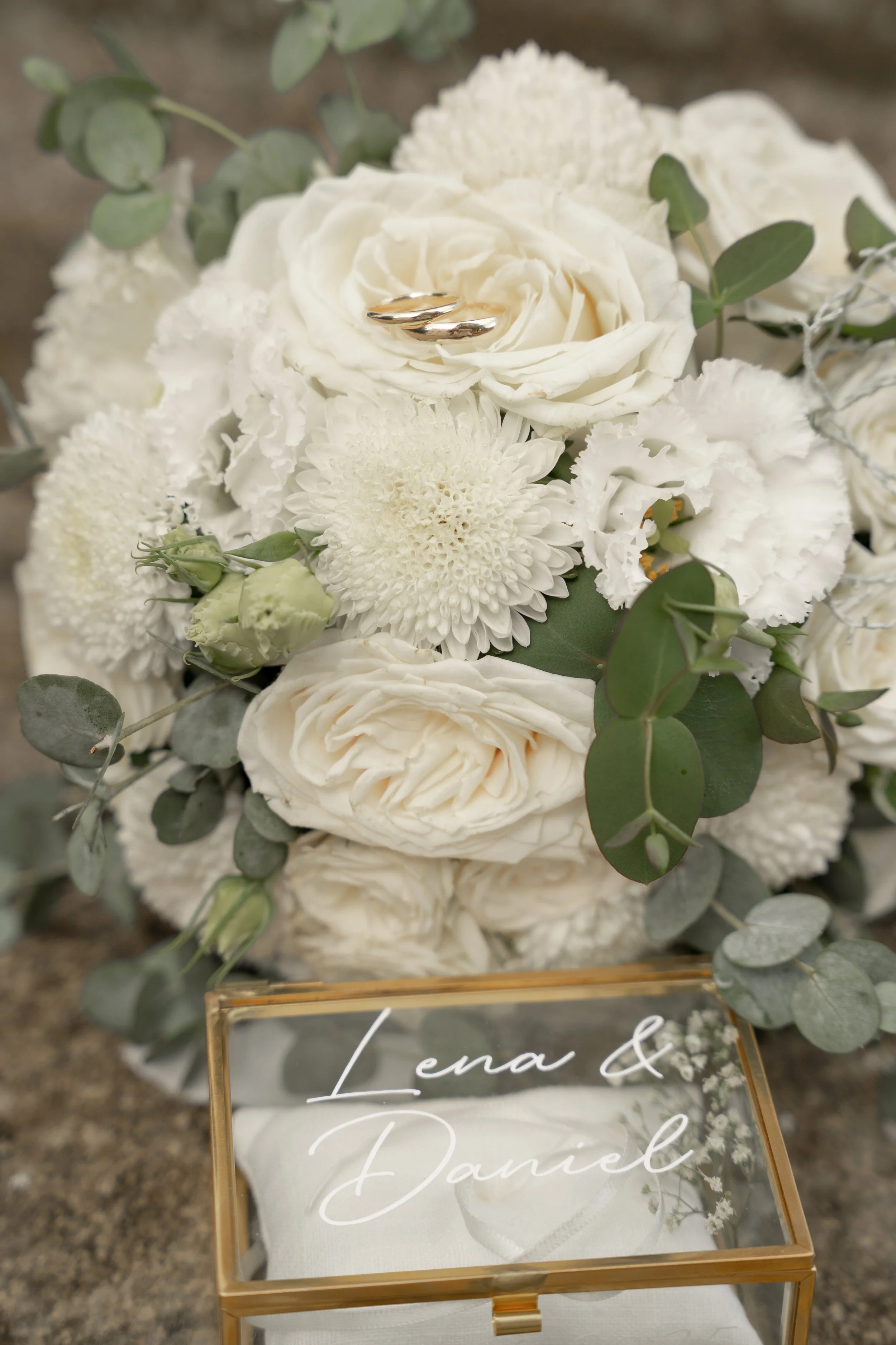 Hochzeitsstrauß aus weißen Blumen mit Eukalyptusblättern und eine Goldbox mit den Namen Lena & Daniel in eleganter Schrift.