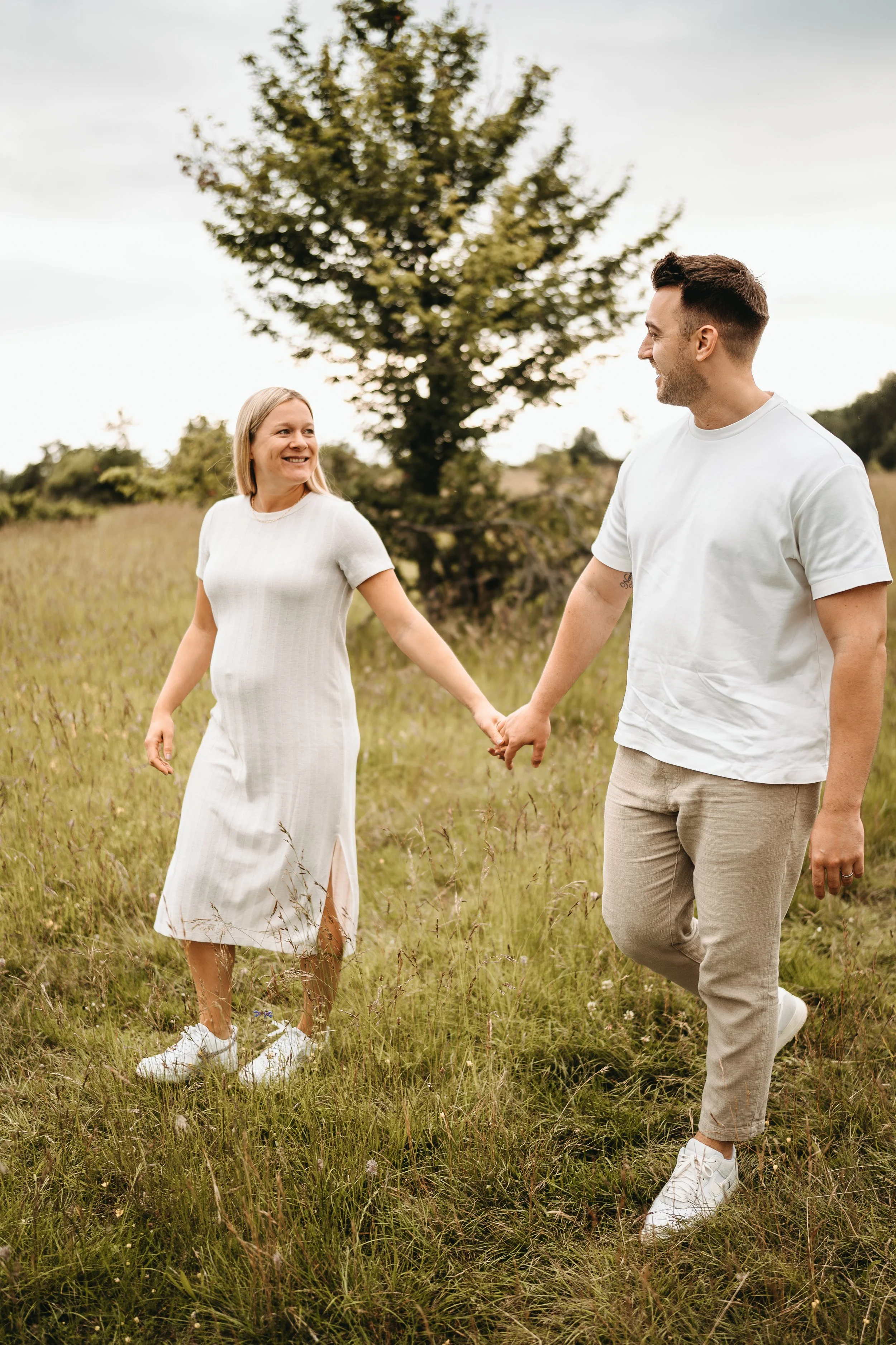 Ein Paar hält Händchen und läuft in einem Feld, lächelnd, bei bewölktem Himmel.
