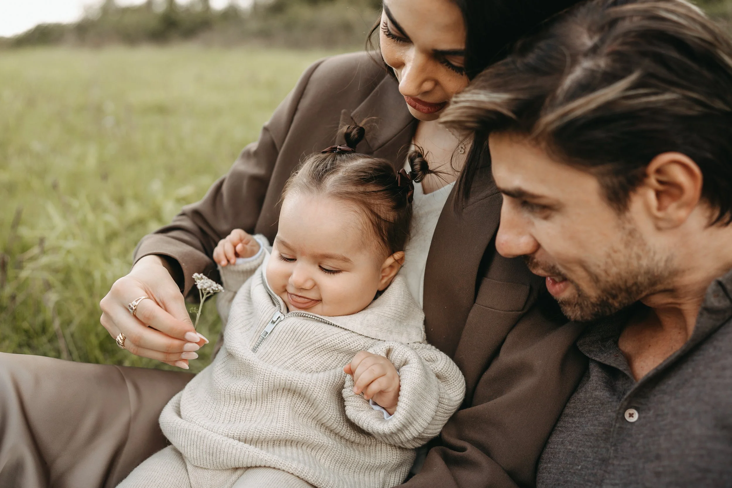Familie sitzt im Freien auf dem Gras, Mutter, Vater und kleines Mädchen, das lachen und spielen.