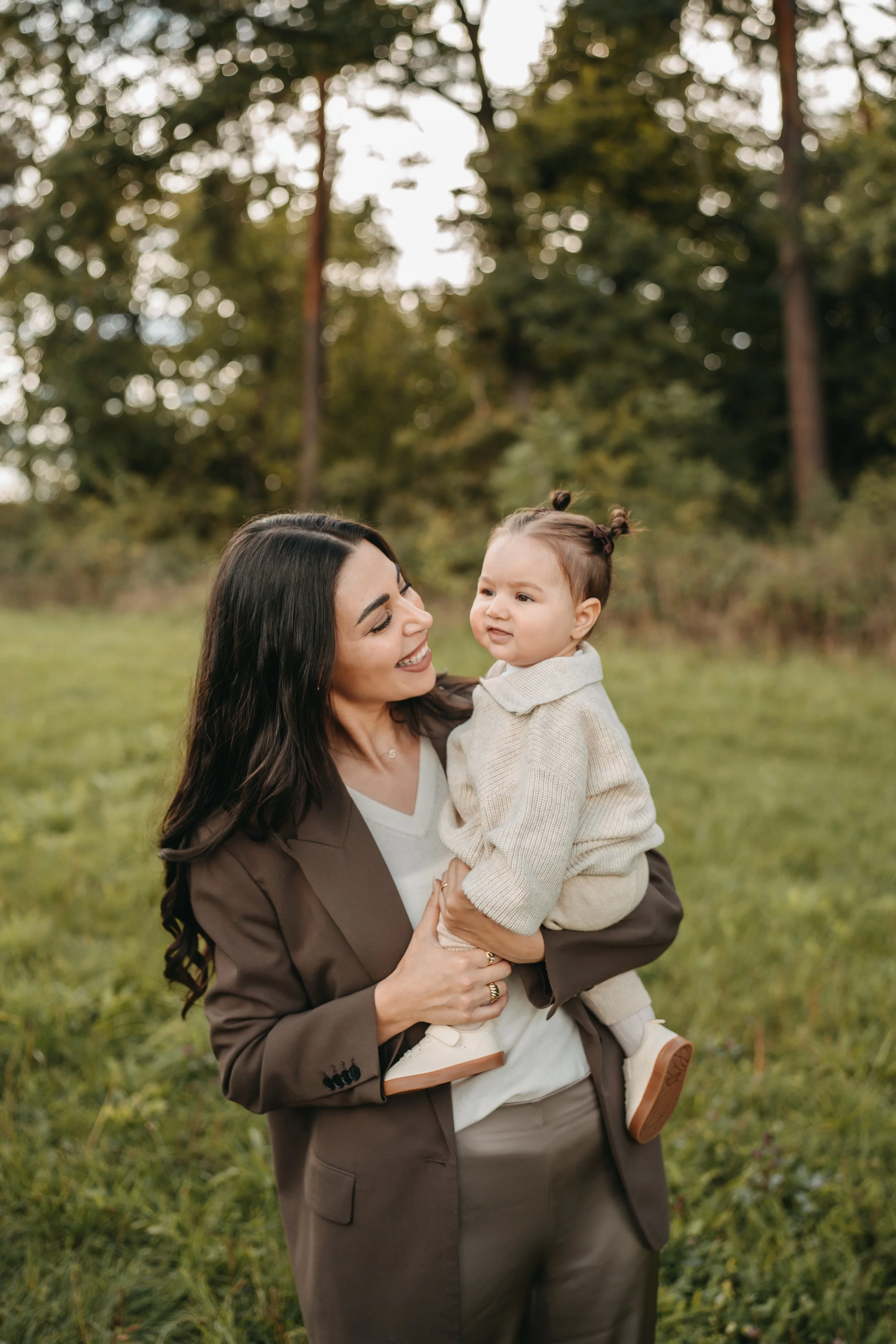Eine Frau hält ein kleines Mädchen im Park, umgeben von Bäumen und Grünflächen, entspannt und freundlich.