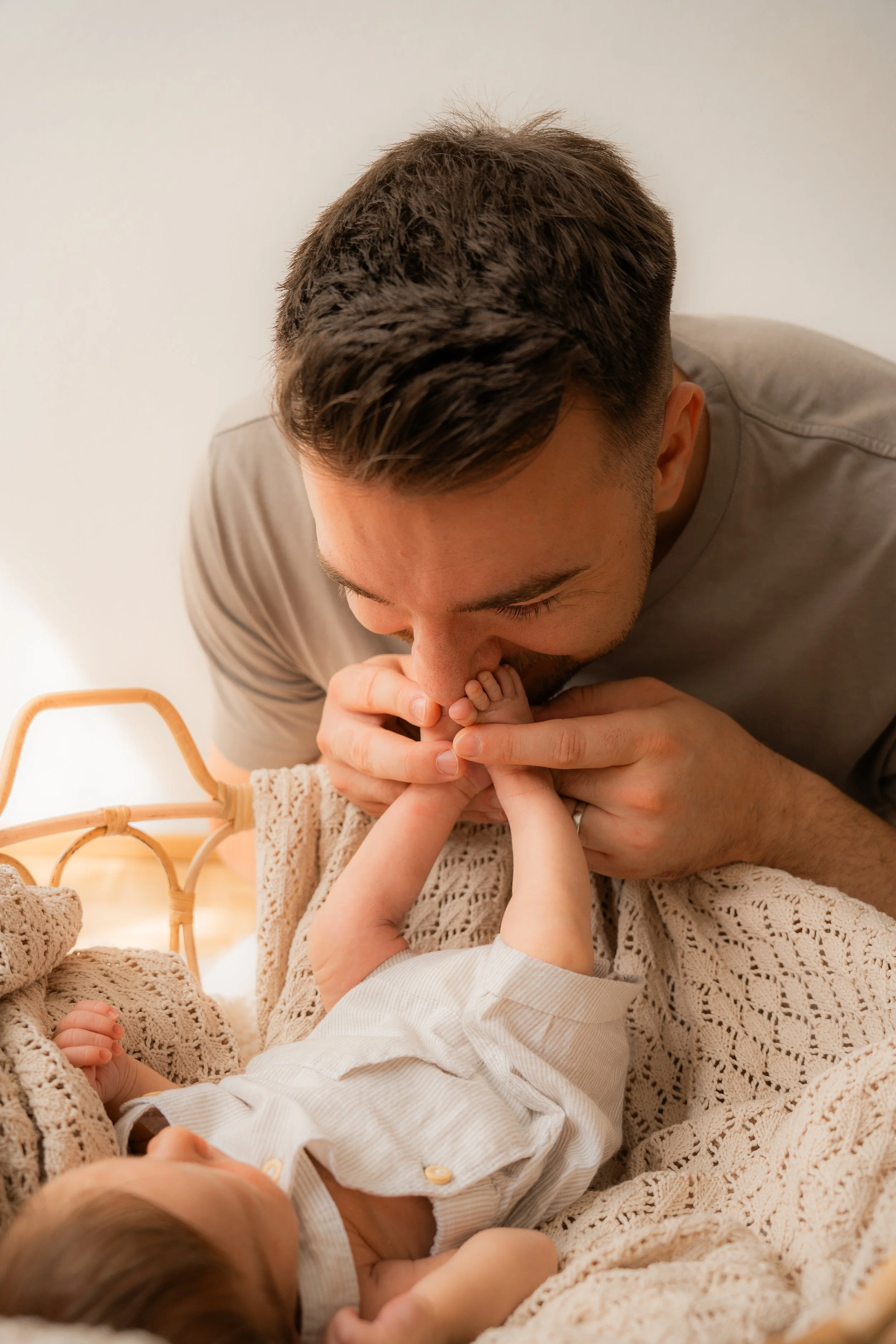 Ein Mann küsst ein Baby auf die Nase, während es auf einem Bett liegt.