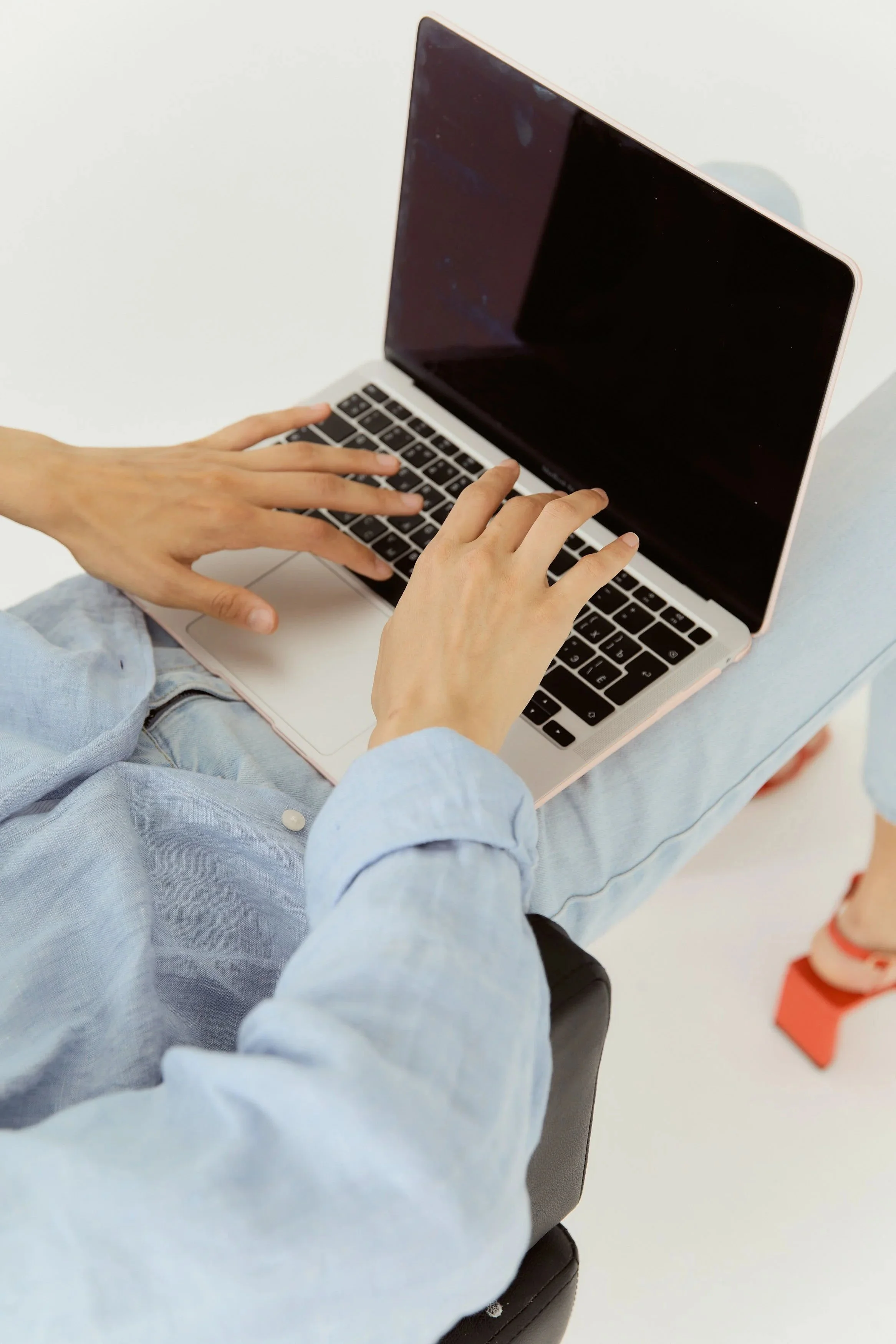 brightivse woman sitting comffortably in chair typing on laptop keyboard wearing denim and orange sandals