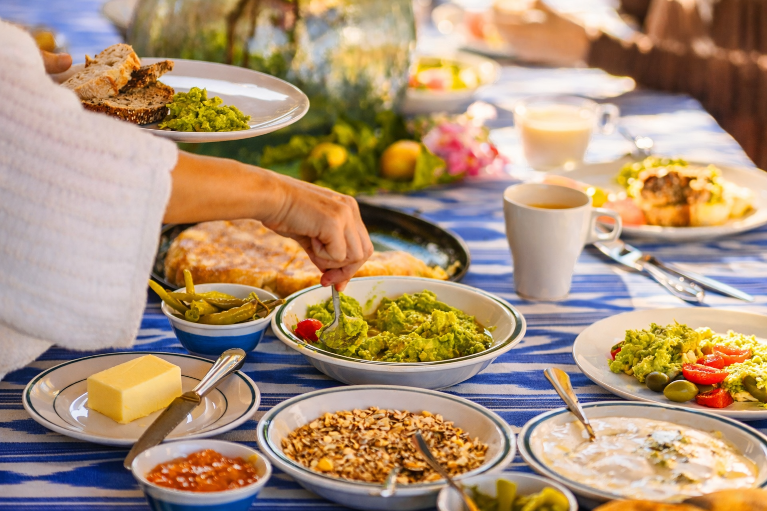 Family outdoor brunch with various dishes including guacamole, salsa, bread, and drinks on a table with a blue and white striped tablecloth.
