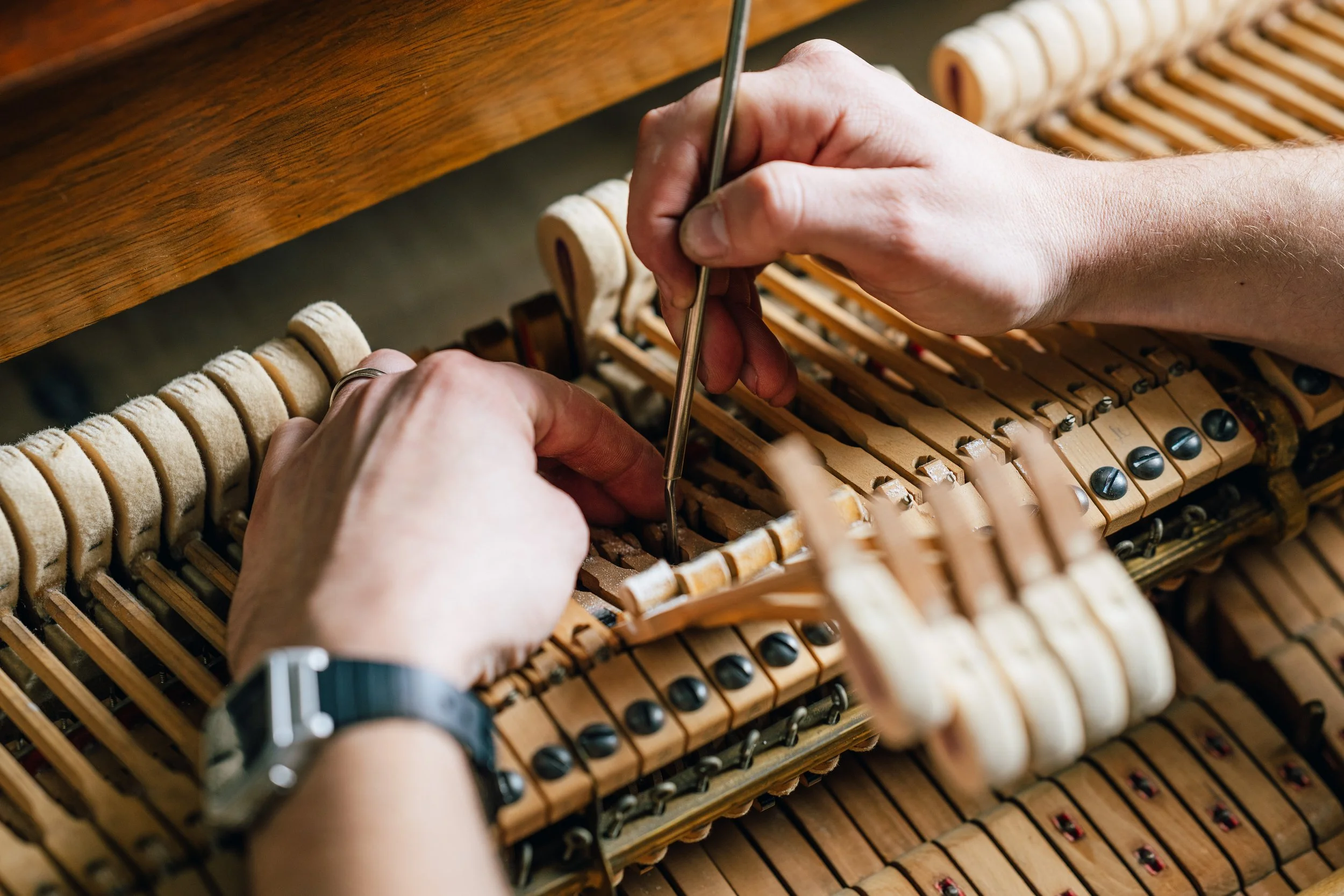 Close-up of hands repairing the internal components of a piano, using a tool to adjust or fix the strings and hammers.