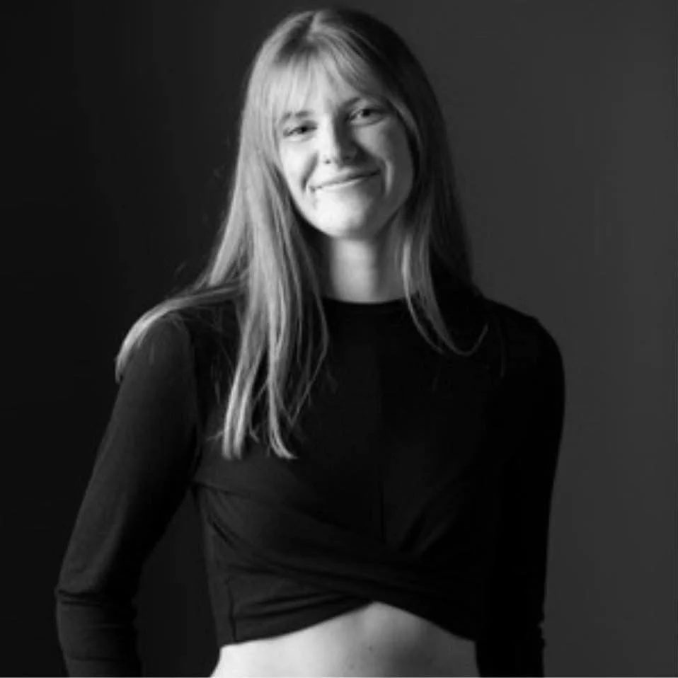 Een zwart-wit foto van een lachende vrouw met lang haar, gekleed in een zwarte top, staand voor een donkere achtergrond.