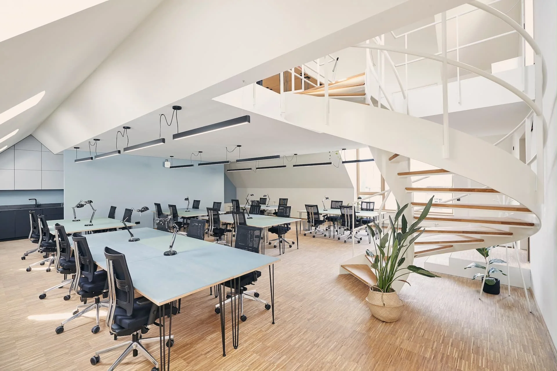 Modernes Büro mit mehreren Arbeitsplätzen, hellen Holztischen, ergonomischen Stühlen und großen Fenstern mit Tageslicht