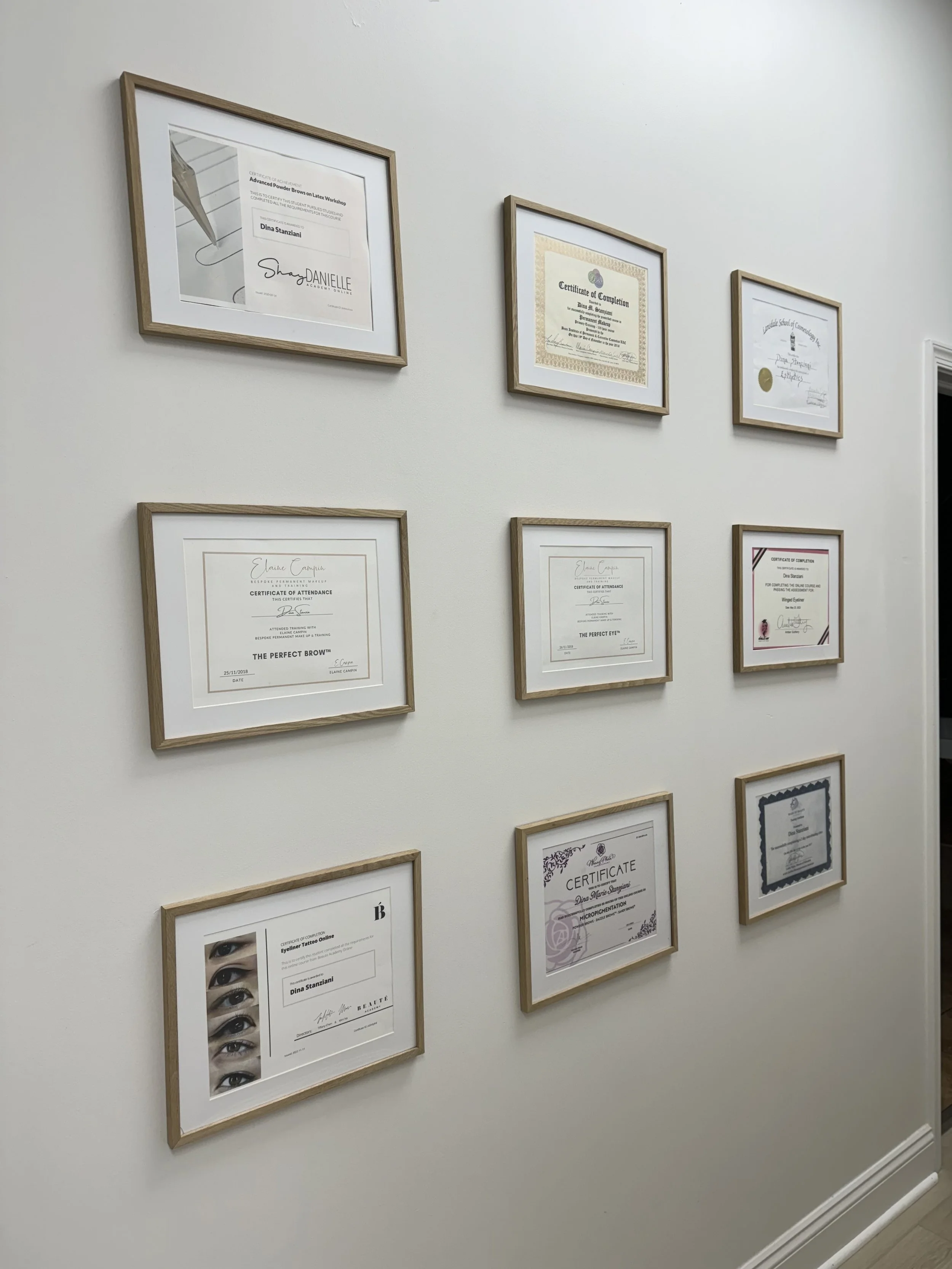 Wall display of various framed certificates and diplomas, arranged in a grid pattern.