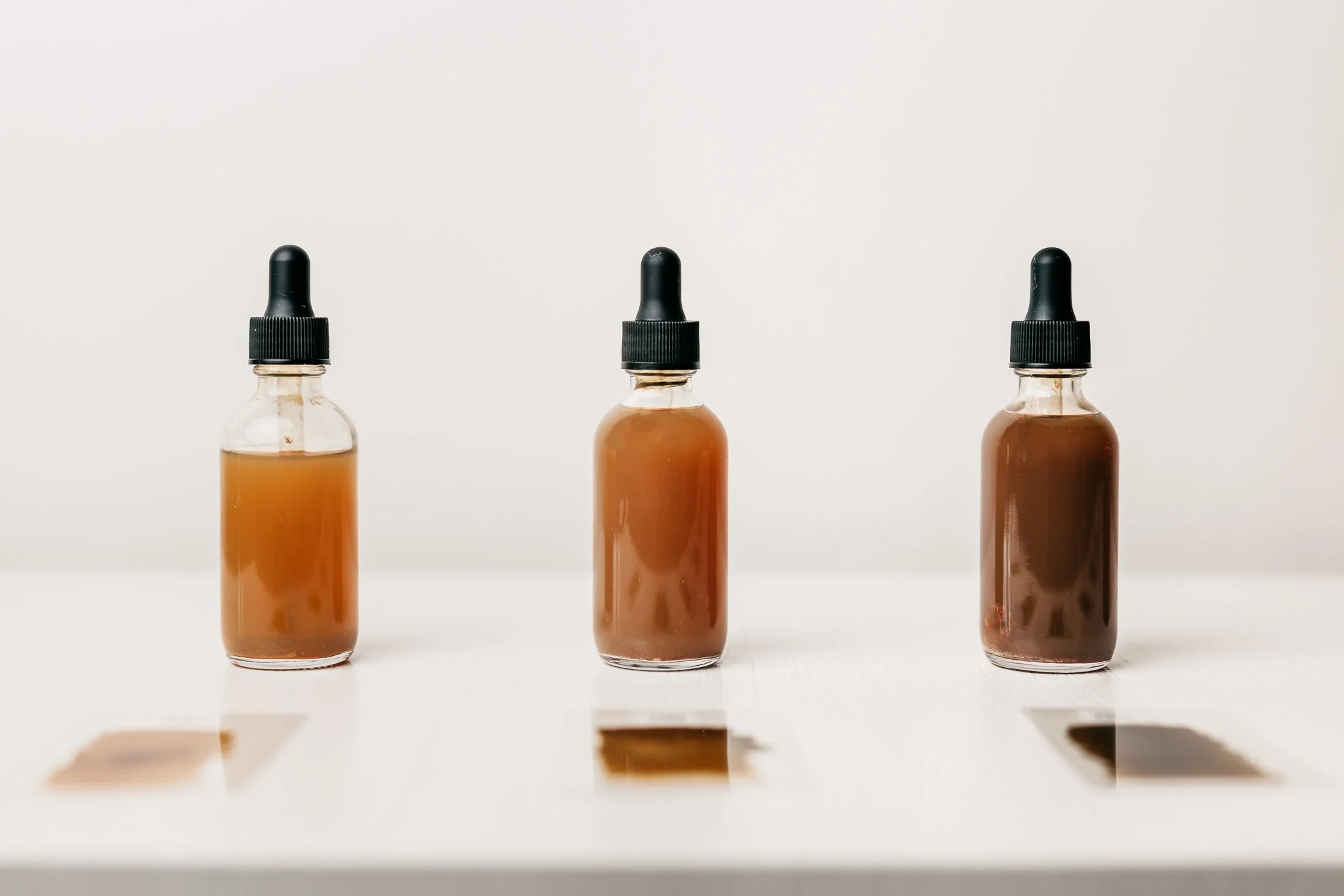 Three glass dropper bottles filled with an amber-colored liquid, arranged in a row on a white surface against a plain white background.
