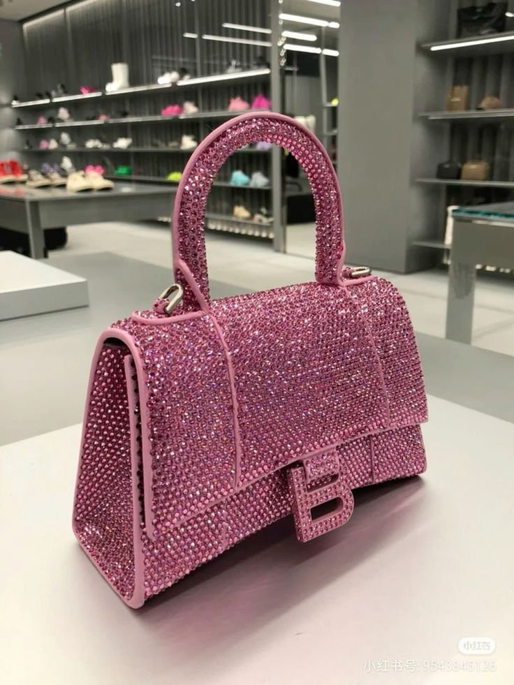 A pink handbag decorated with rhinestones, displayed on a store counter with shelves of shoes in the background.