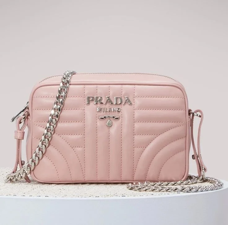 A pink Prada Milano handbag with a silver chain strap and logo, displayed on a white surface against a light background.