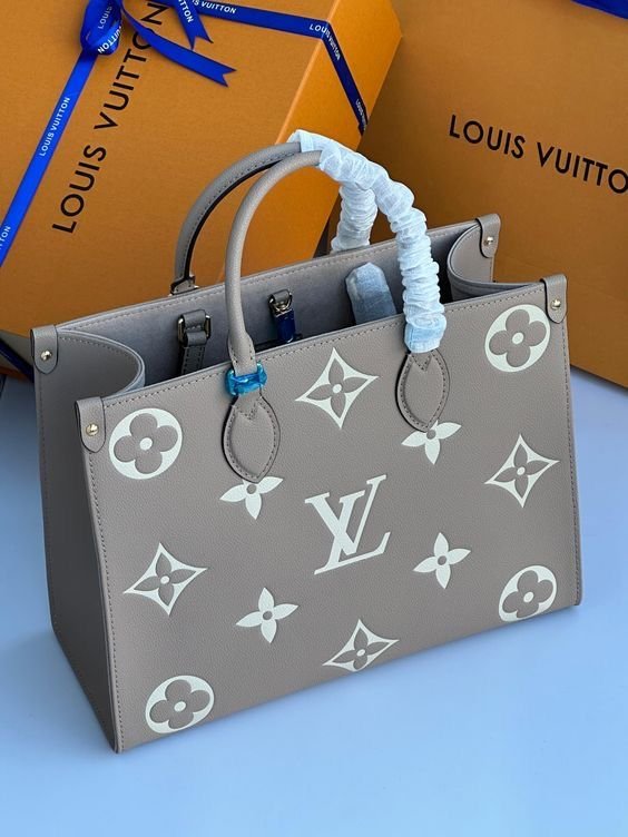 A gray Louis Vuitton handbag with white floral and monogram patterns, wrapped handles, and Louis Vuitton shopping boxes in the background.