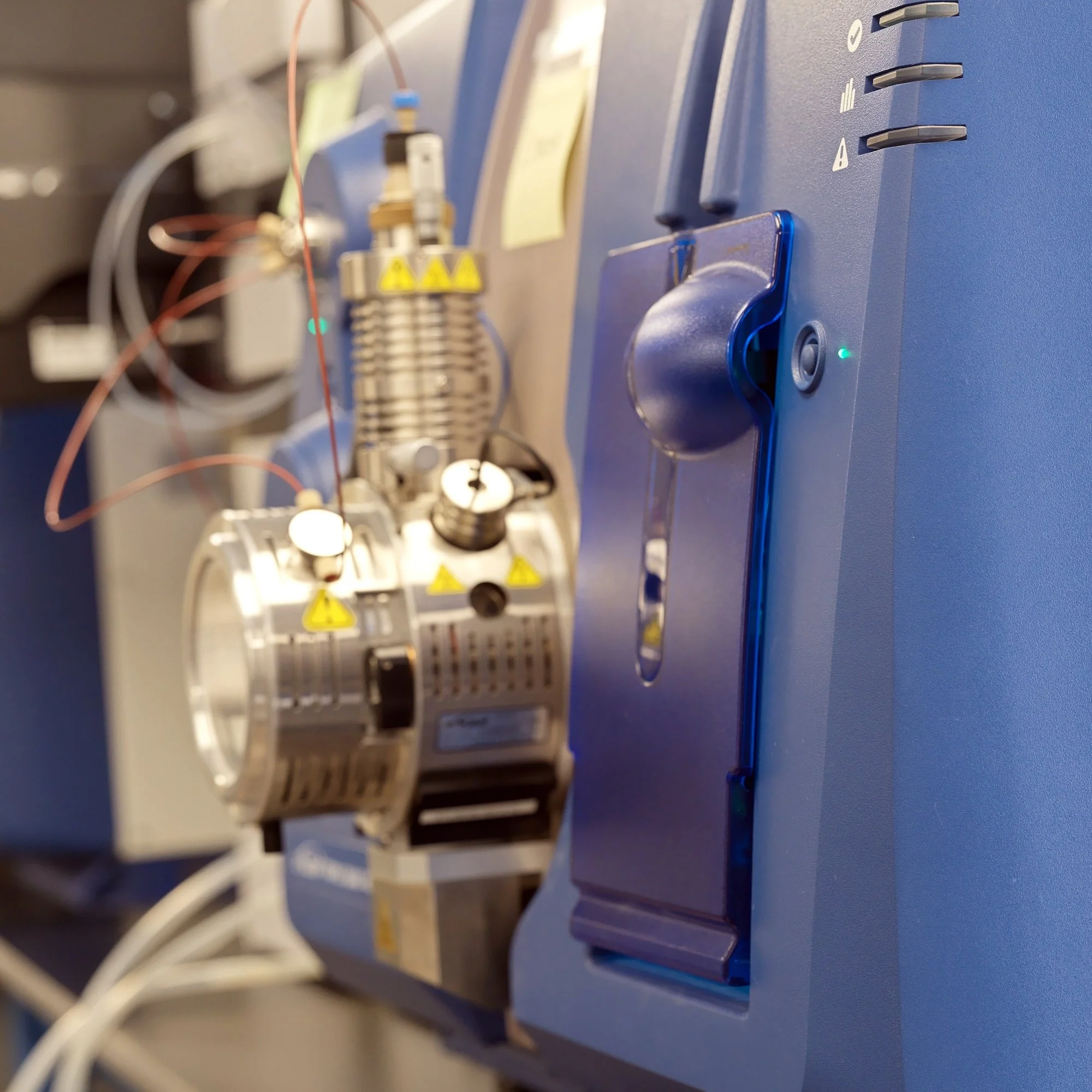 Close-up view of laboratory equipment with digital controls, wires, and warning labels, used in scientific experiments.