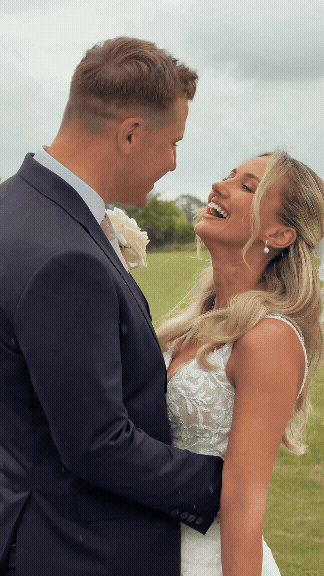 A bride and groom smiling and looking at each other outdoors on a cloudy day