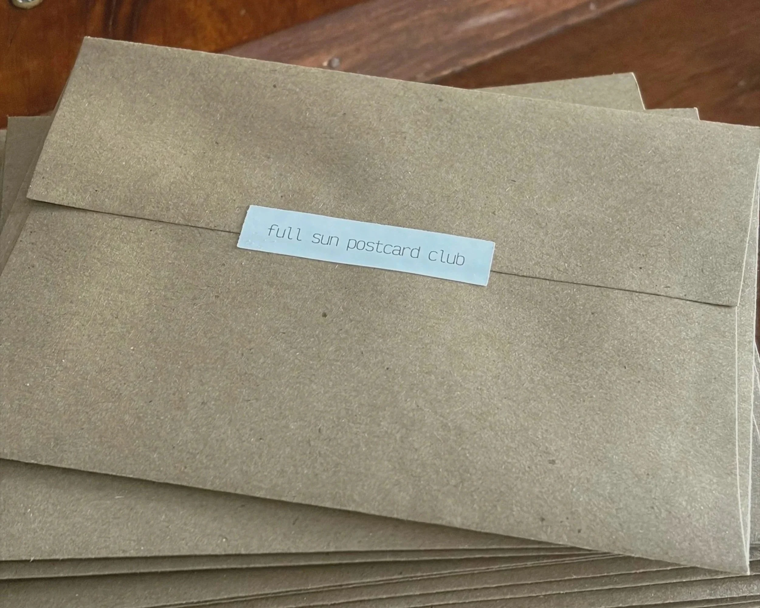 Stack of brown envelopes with a label that reads 'full sun postcard club' in lowercase letters.