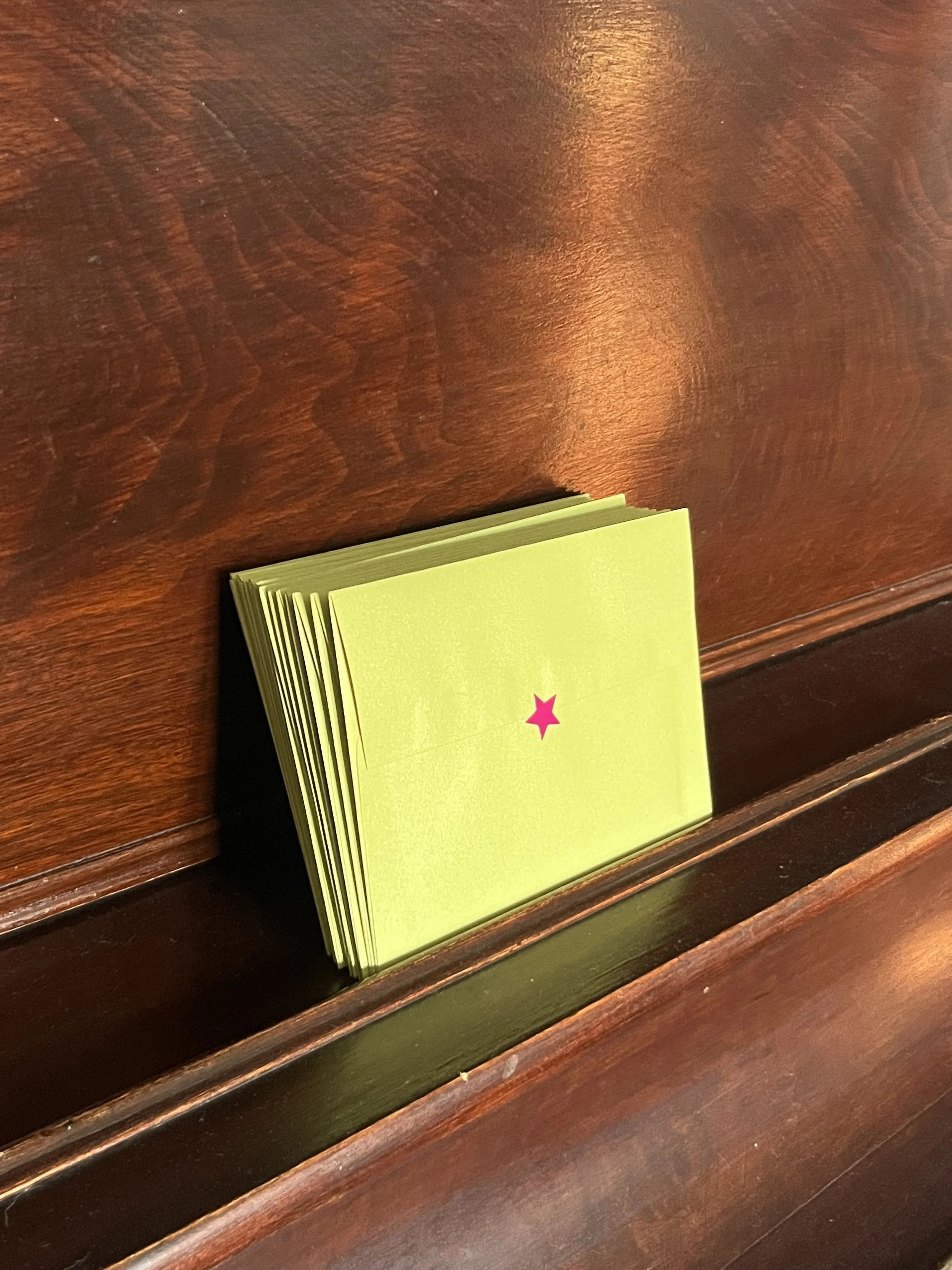 A stack of green cards with a pink star in the center, placed on a wooden surface.
