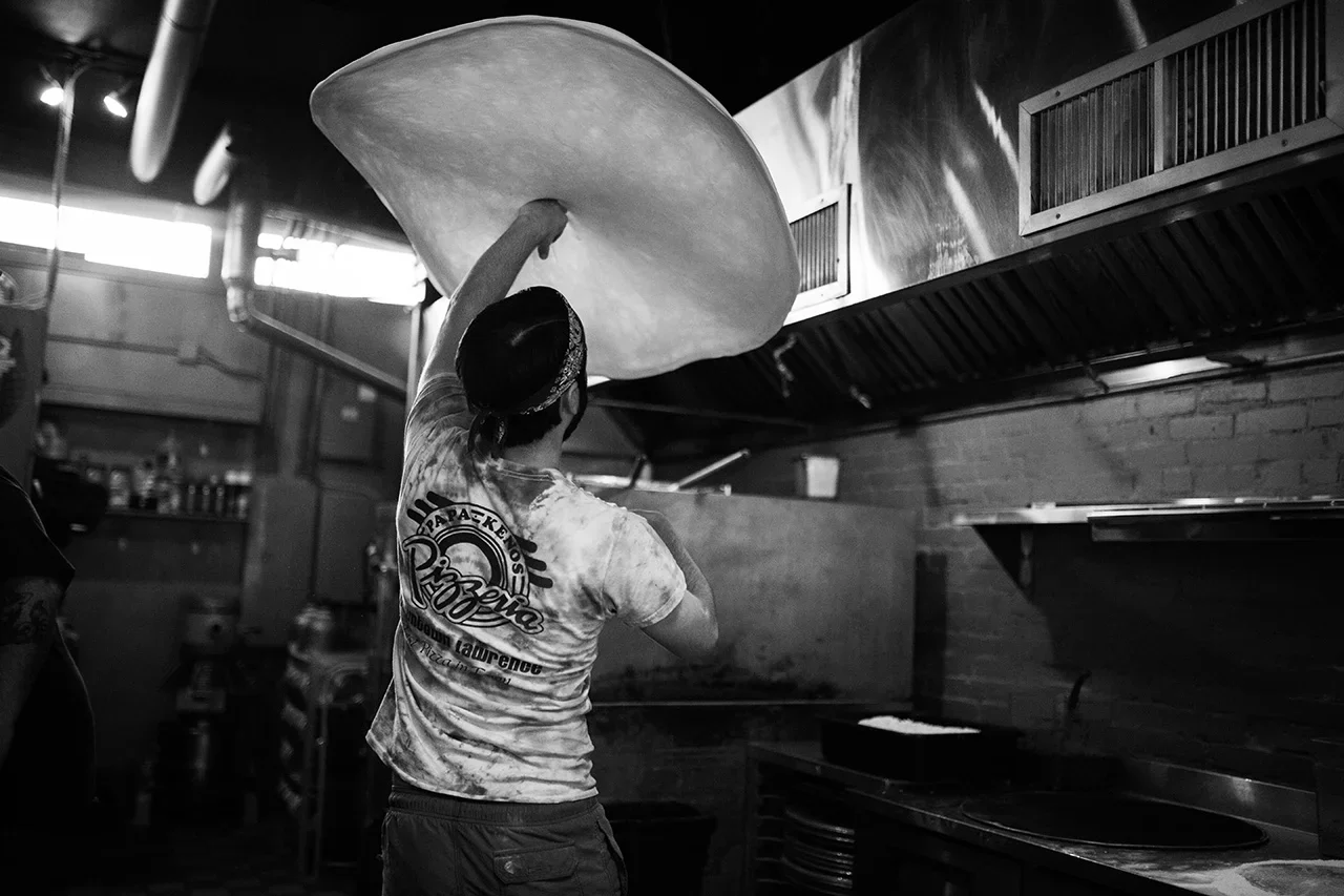 Person tossing pizza dough in a kitchen