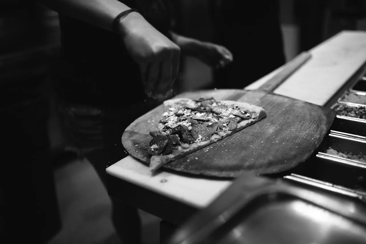 A person preparing a pizza on a wooden paddle in a kitchen.