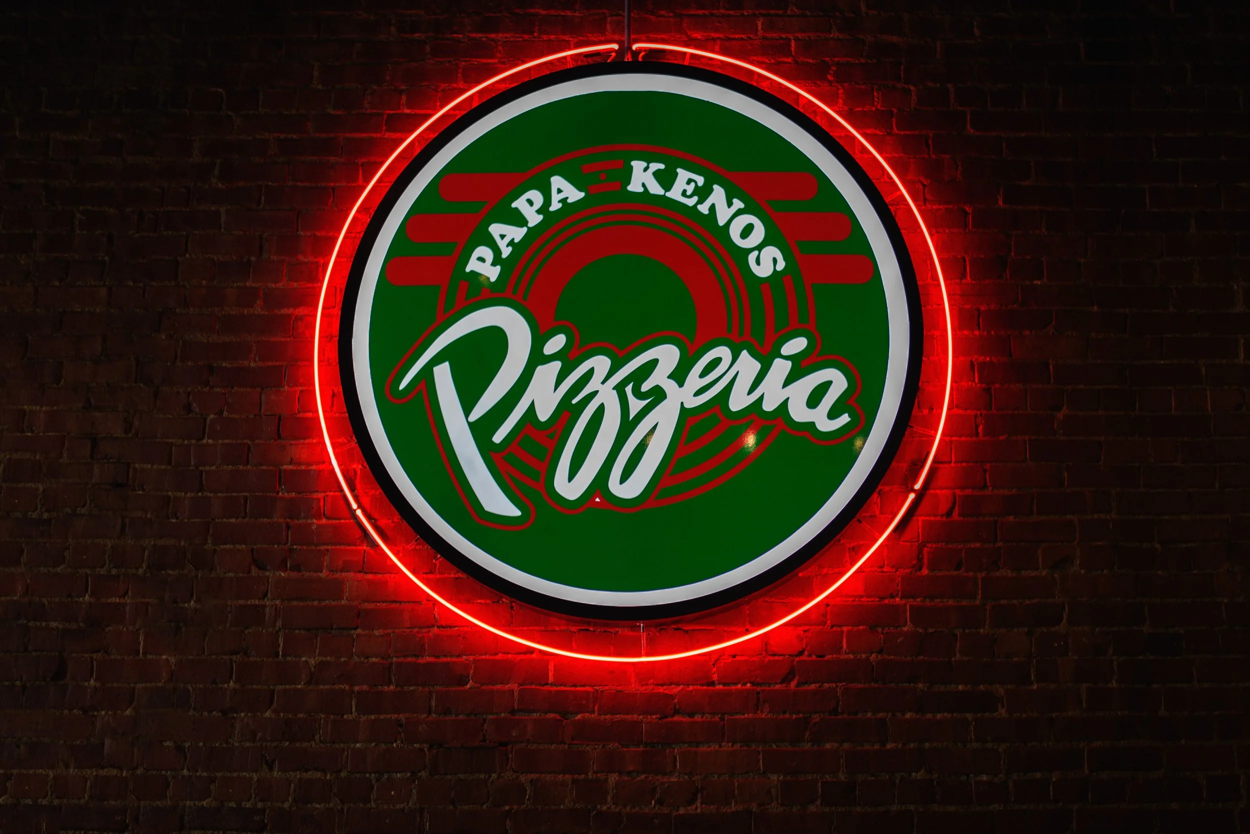 Neon sign of Pizza logo with red, green, and white colors, mounted on a brick wall.