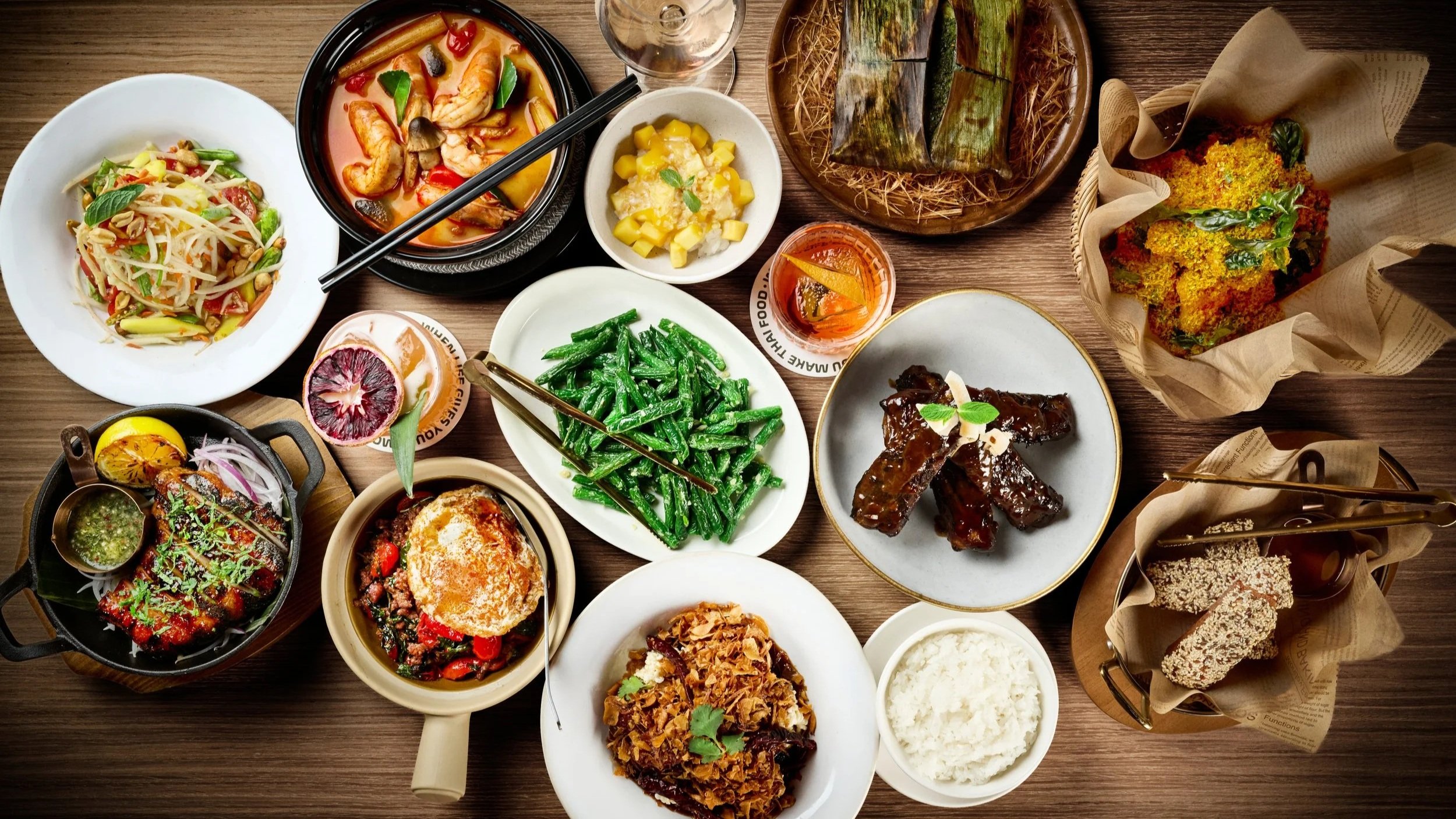 A full table of signature Thai dishes featuring grilled meats, stir-fried vegetables, and traditional sides, showcasing a vibrant and authentic Thai dining spread in LA Very Thai Westfield Century City.
