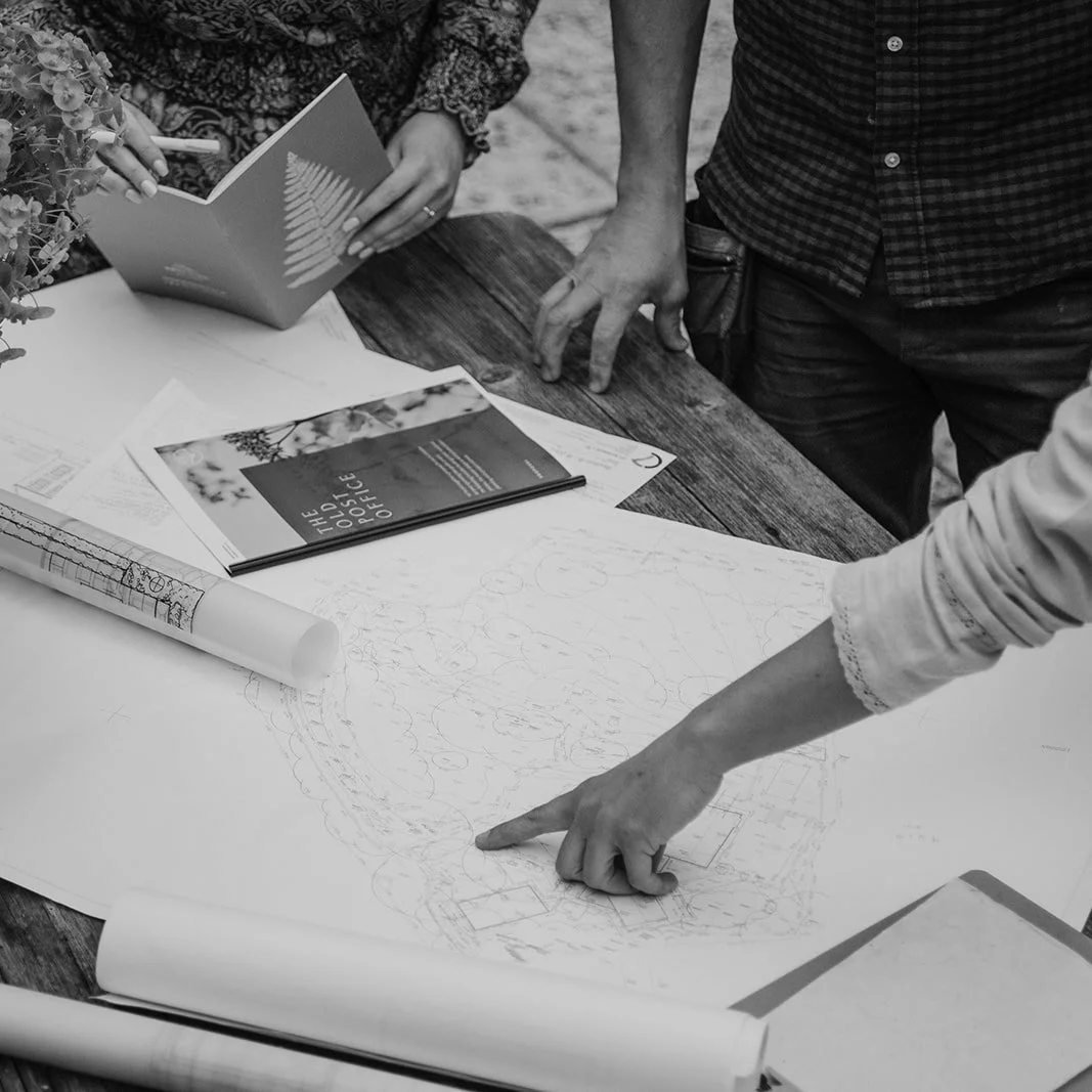 People reviewing landscape plans and documents on a wooden table, with detailed diagrams and informational brochures.