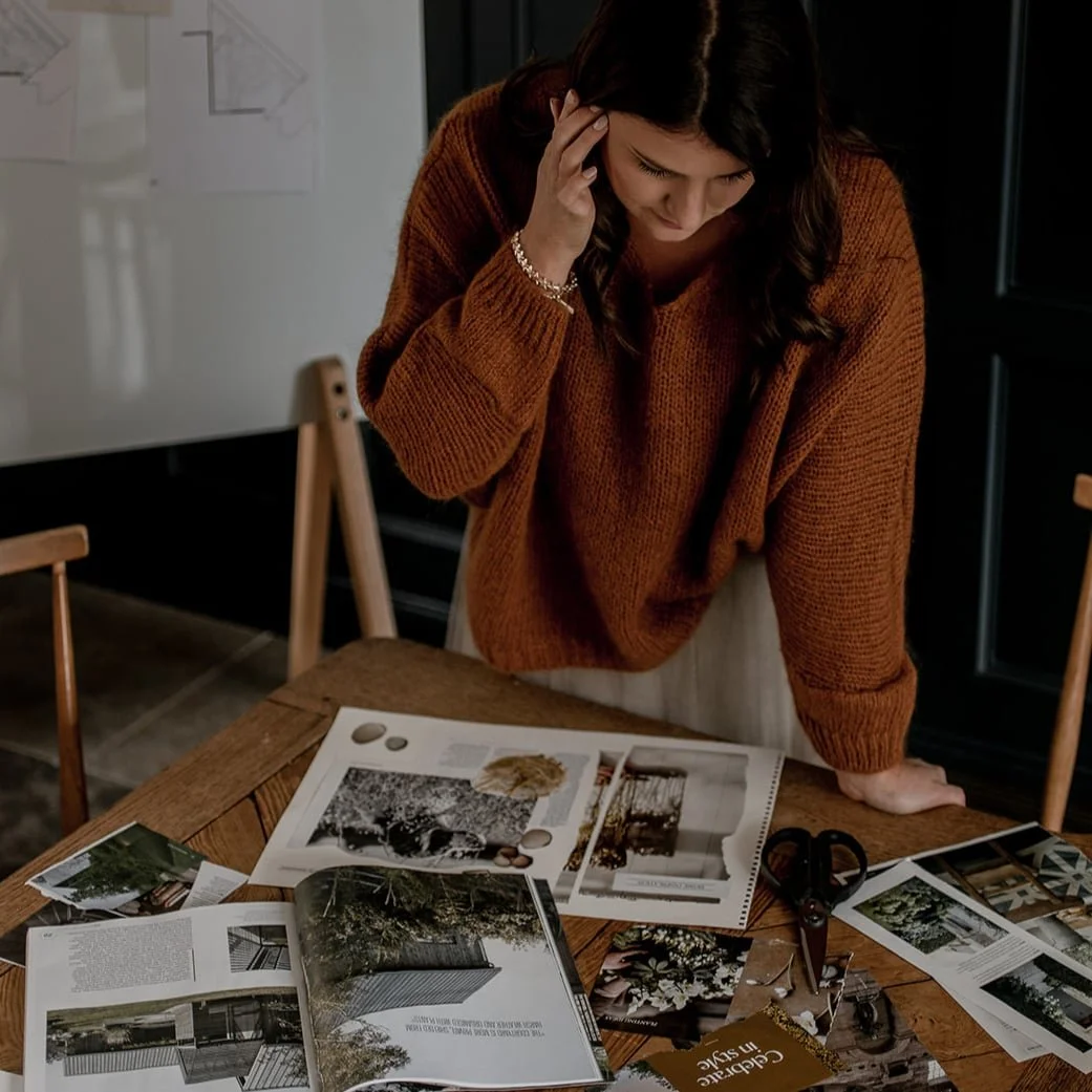 Diane Samways in an orange sweater looks down at a table with magazines, papers, and scissors, appearing to be planning or designing something.