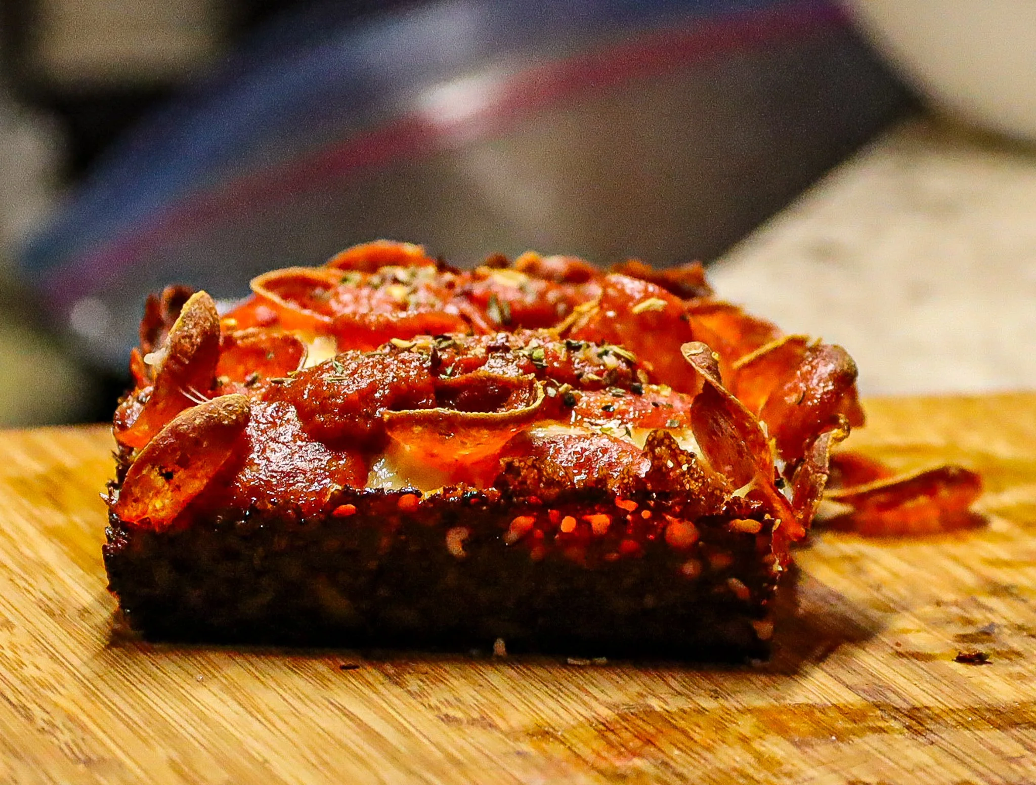 Slice of pepperoni and cheese pizza with crispy crust on wooden cutting board.