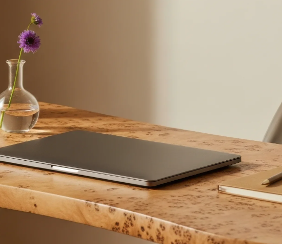 Closed gray laptop on a wooden desk with a small vase of purple flowers and a notebook with a pen.