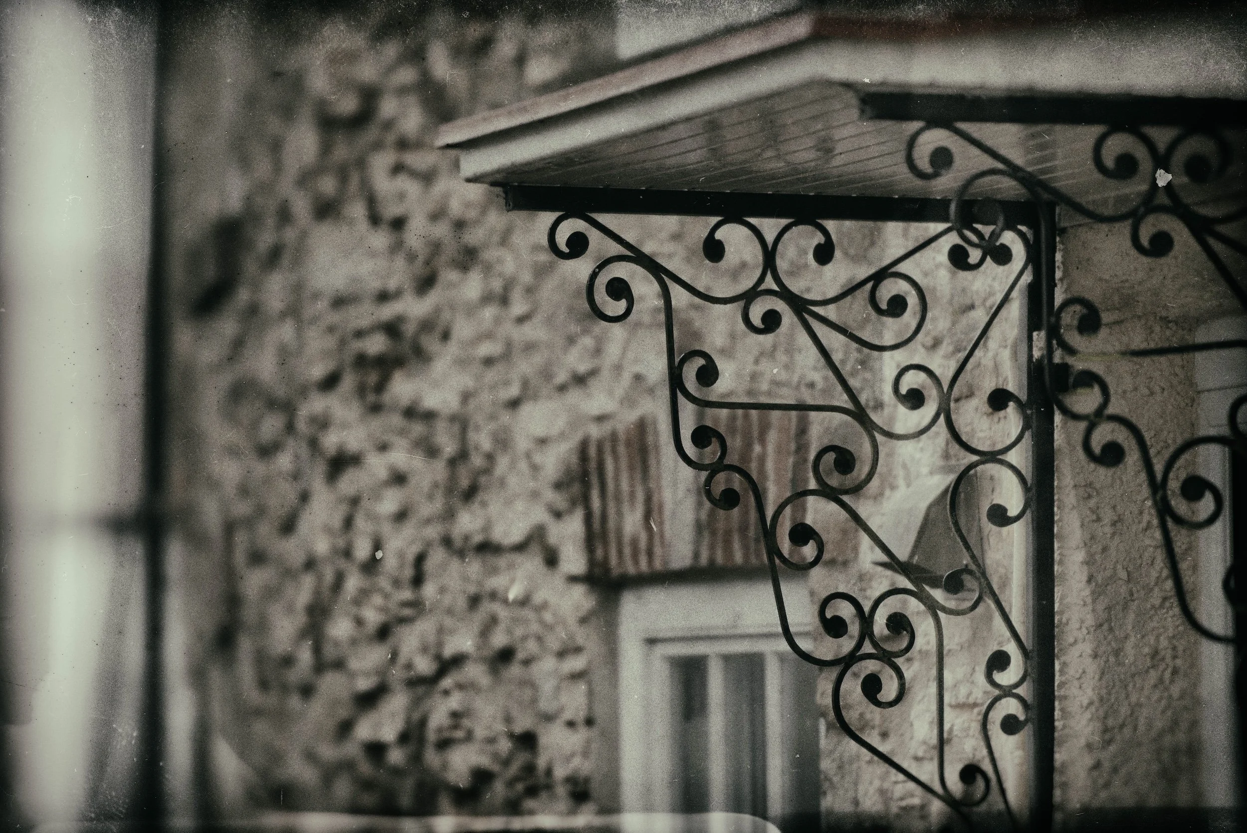 Black decorative wrought iron staircase railing with a wooden staircase above, against a textured wall.