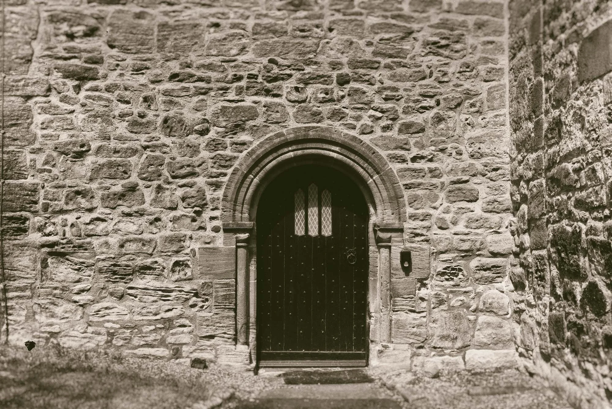 Photograph of a stone wall with an arched wooden door and a small window in the center.