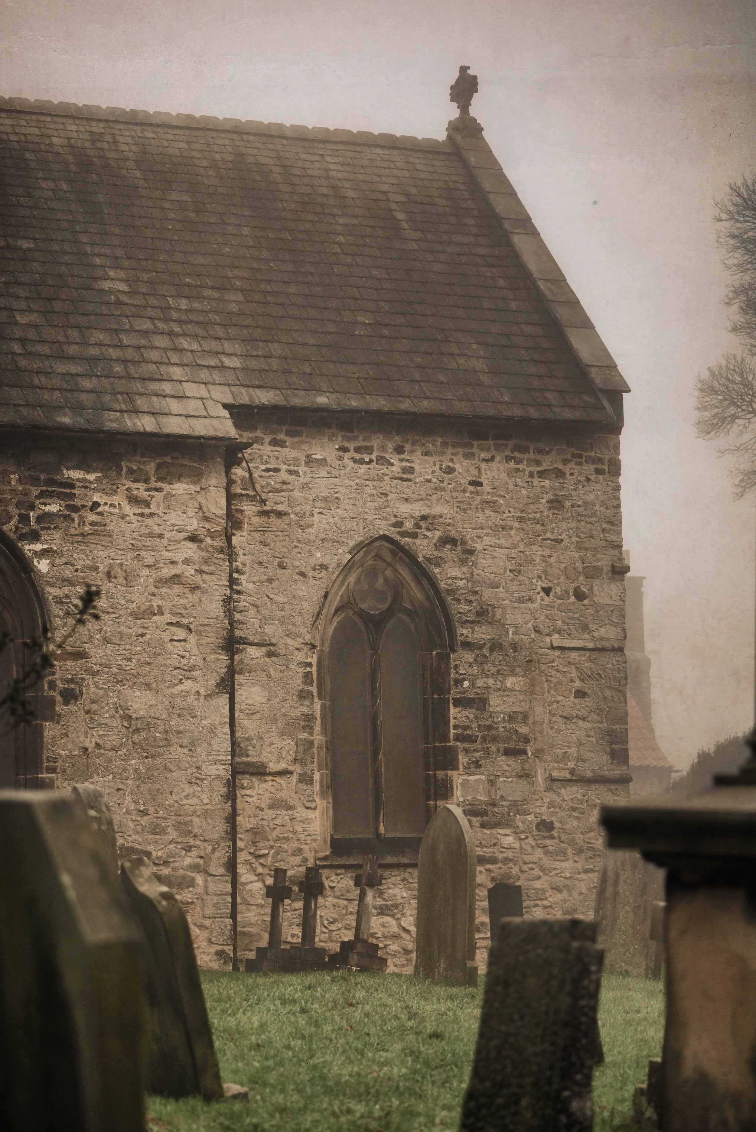 A stone church with tall, arched windows in a graveyard with old tombstones, surrounded by a foggy atmosphere.
