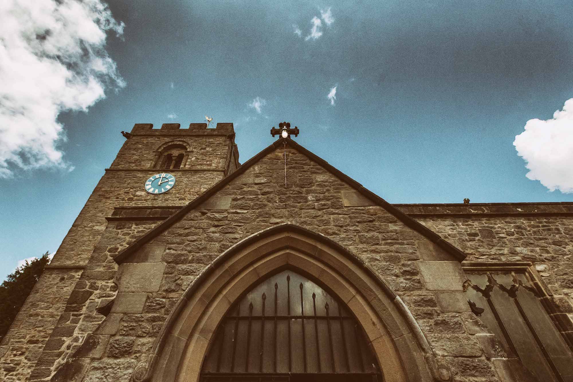 View of St. Michael's Church with a clock tower and pointed arch entrance, under a blue sky with clouds.