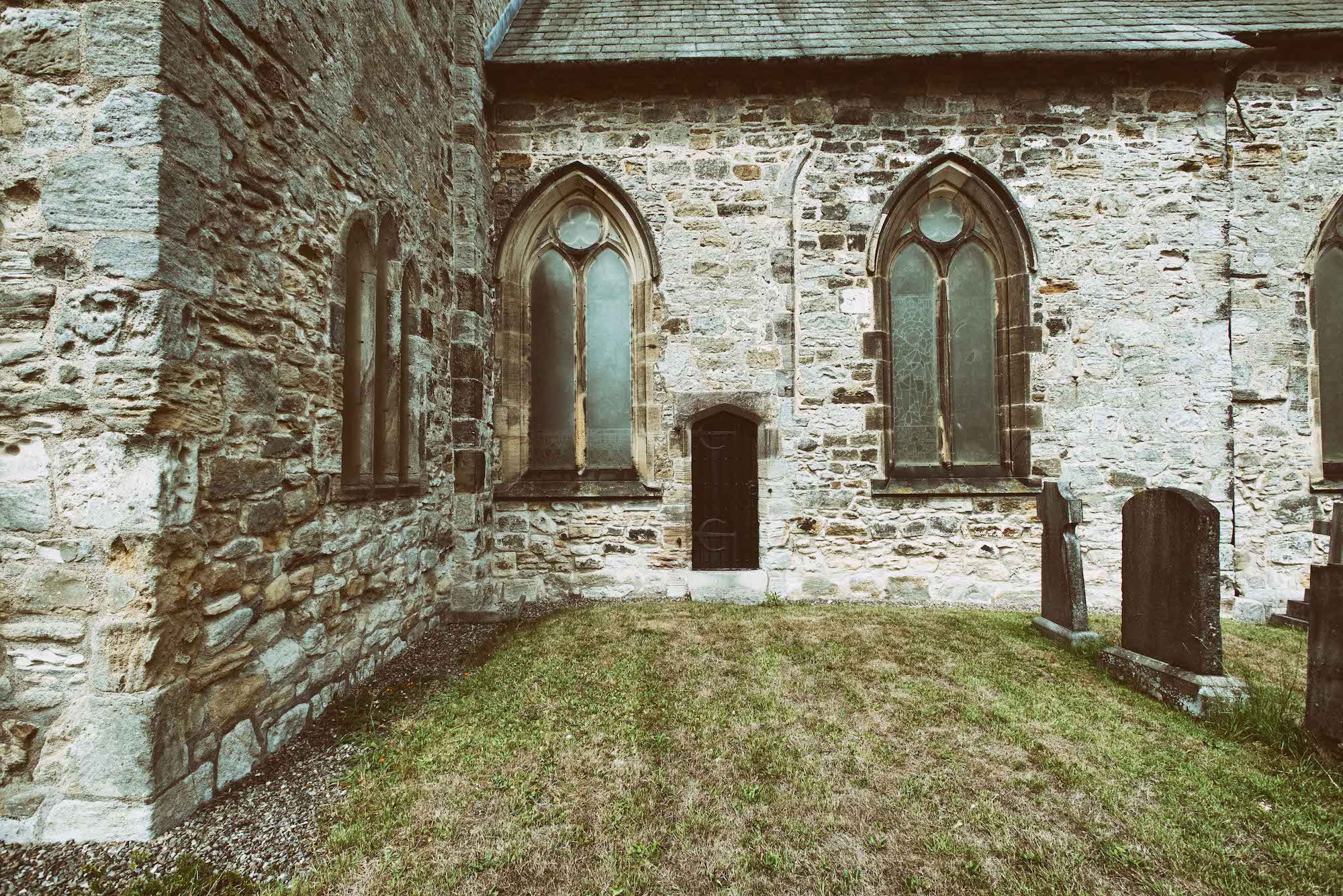 Front view of St. Michael's Church with arched stained glass windows and a small grassy yard with tombstones.