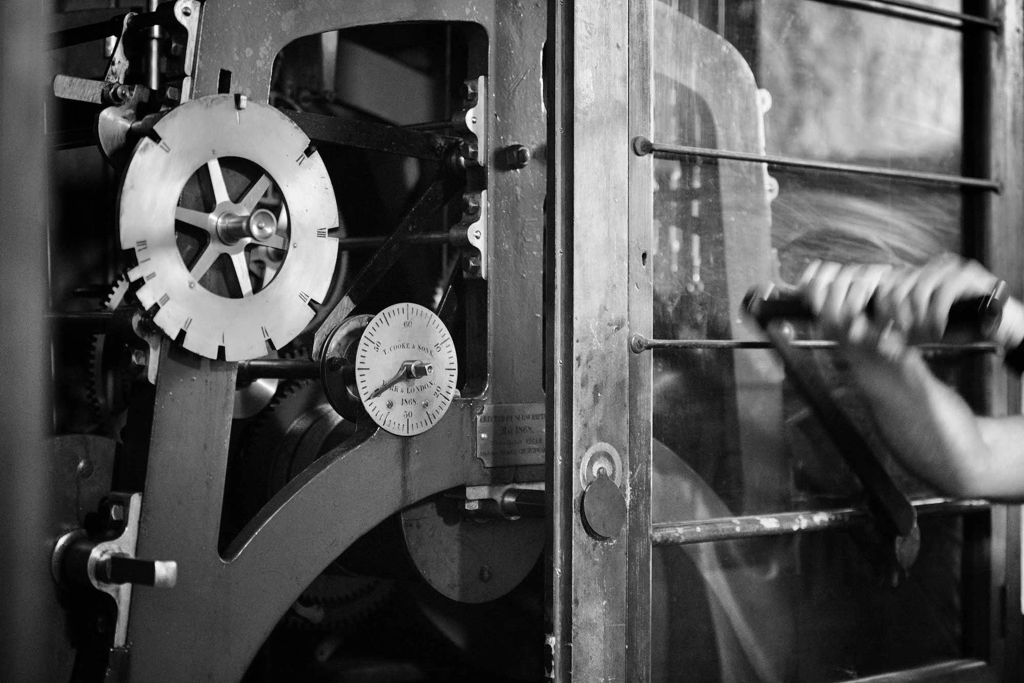 Close-up of an antique clock movement with gears, levers, and a dial marked with Roman numerals and 'T. Cooke & Sons, London, 1868'.