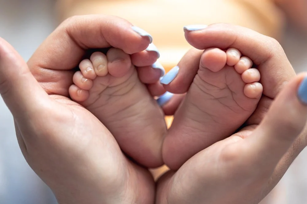 Adult hands holding a baby's feet, forming a heart shape.