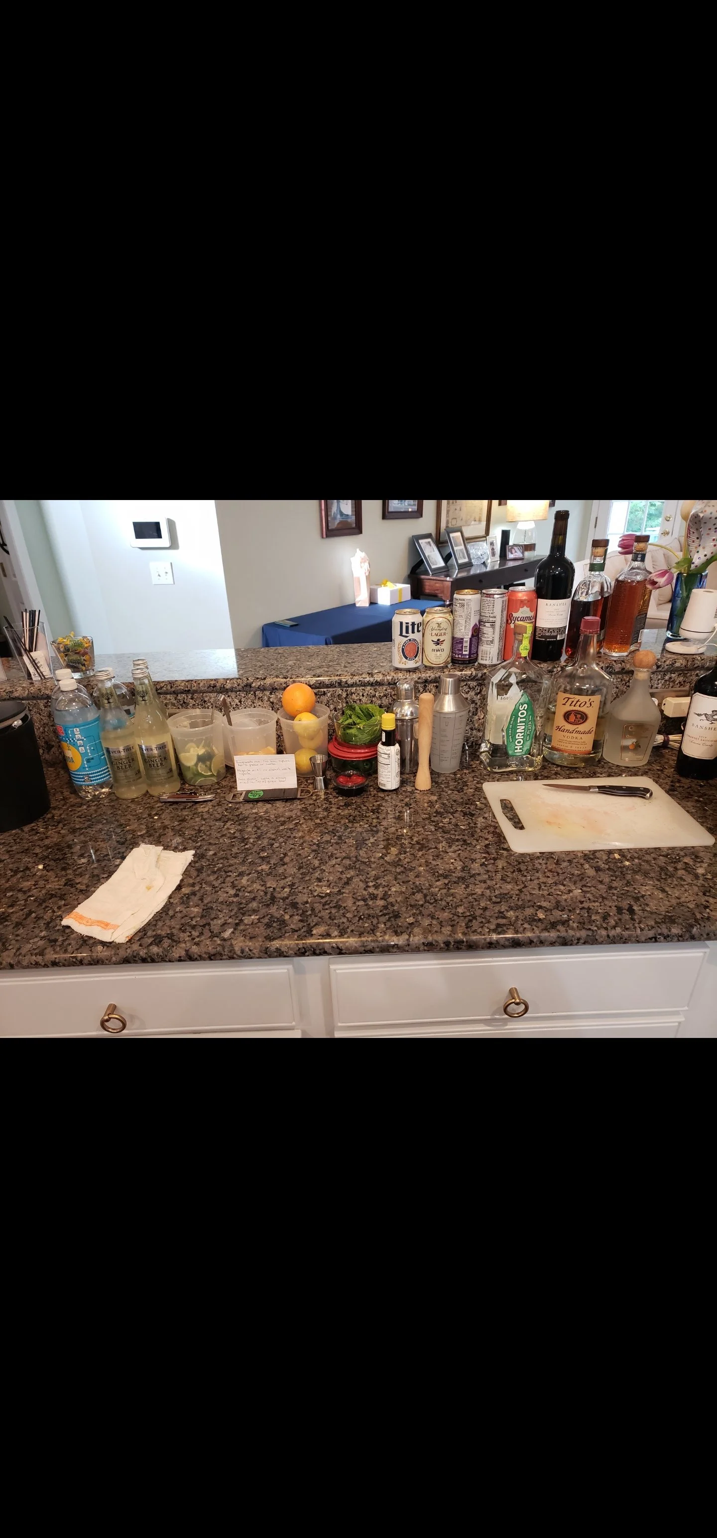 Kitchen counter with various drink bottles, a cutting board, citrus fruits, and kitchen utensils.