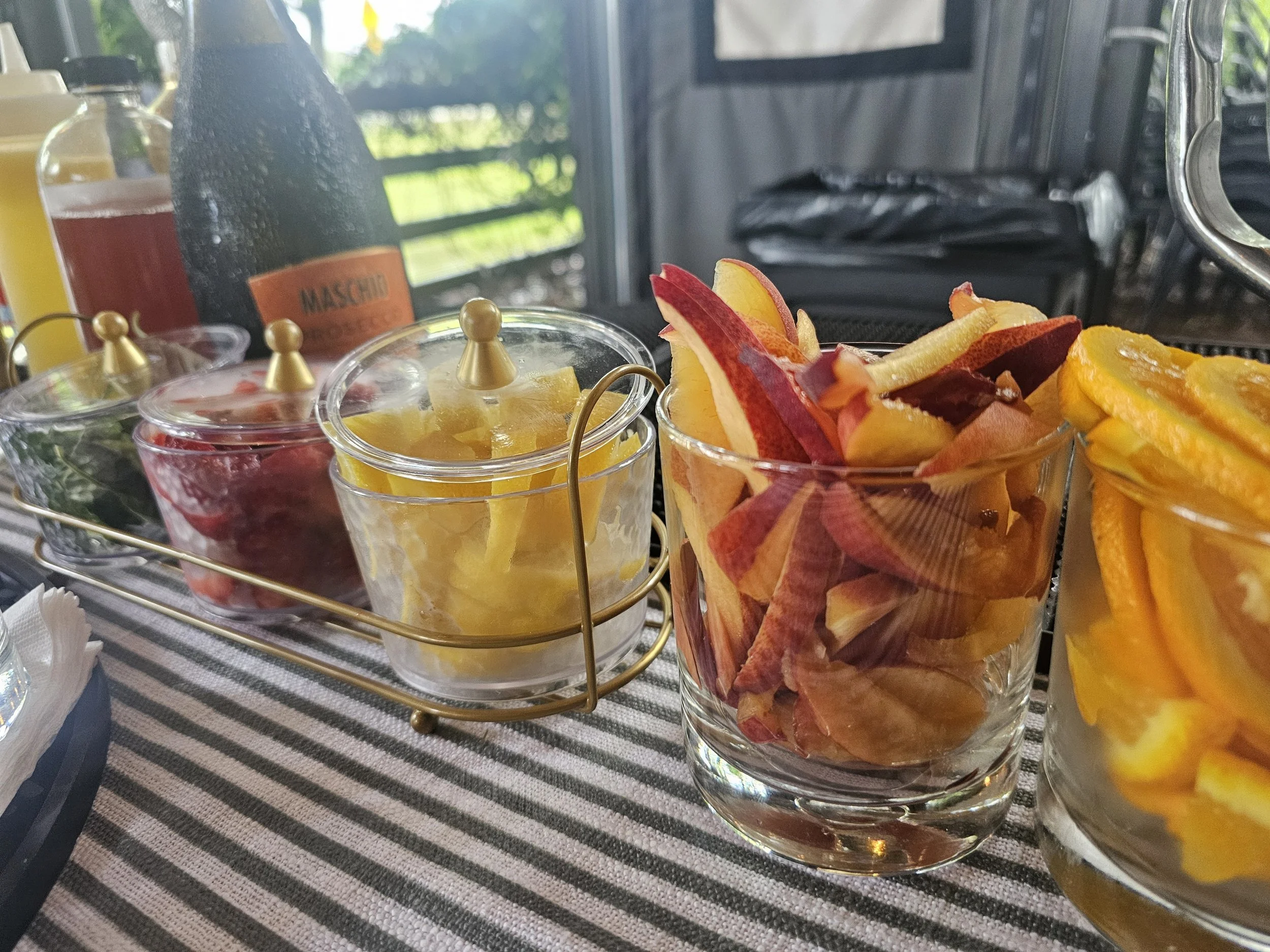 Glass jars filled with sliced fruits and citrus peels, placed on a striped cloth table.