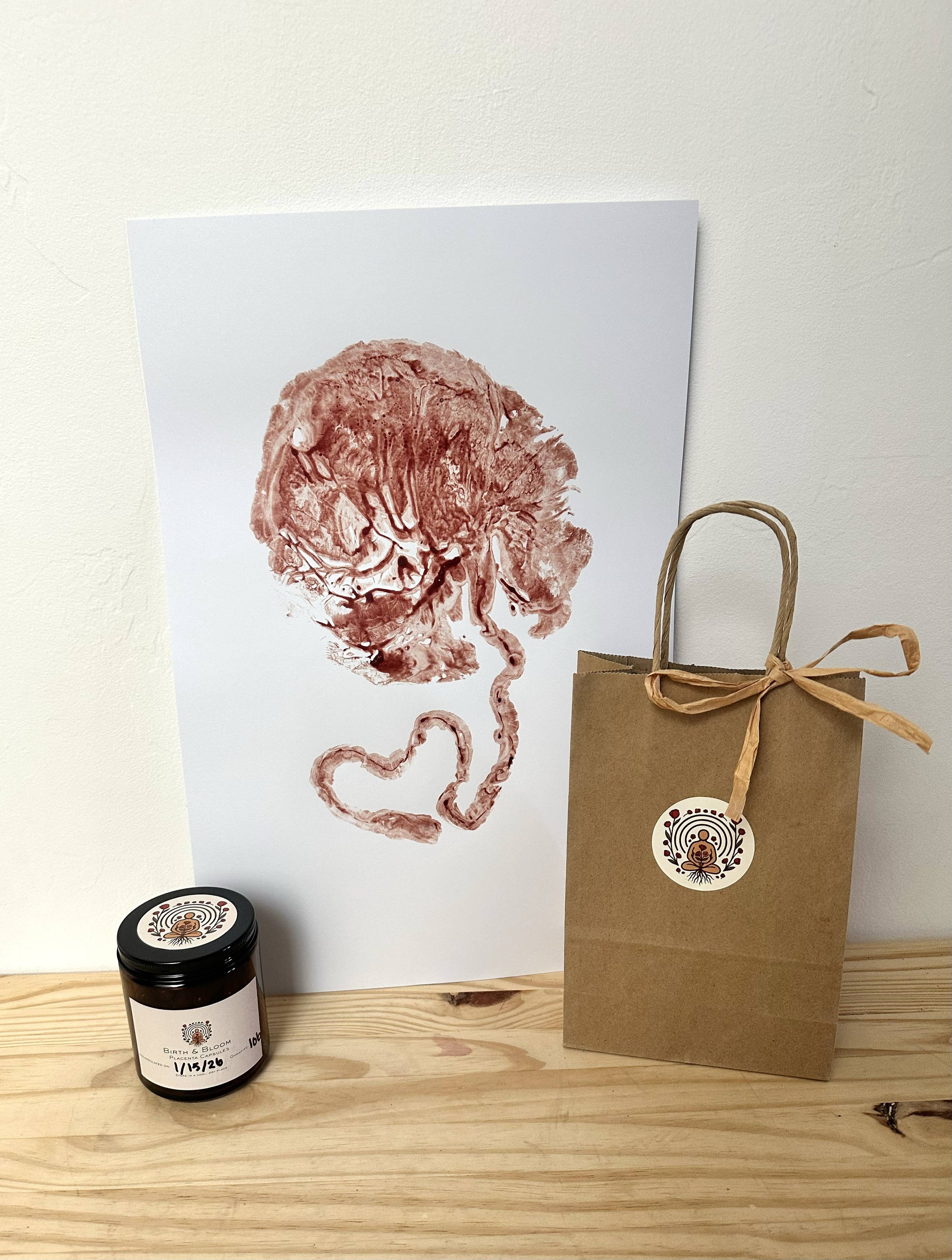 Photo of a placenta print made with blood, a brown glass jar of placenta capsules, and a Birth and Blood Placenta Encapsulation & Doula Services brown gift bag. 
Elise Smith Tucson AZ