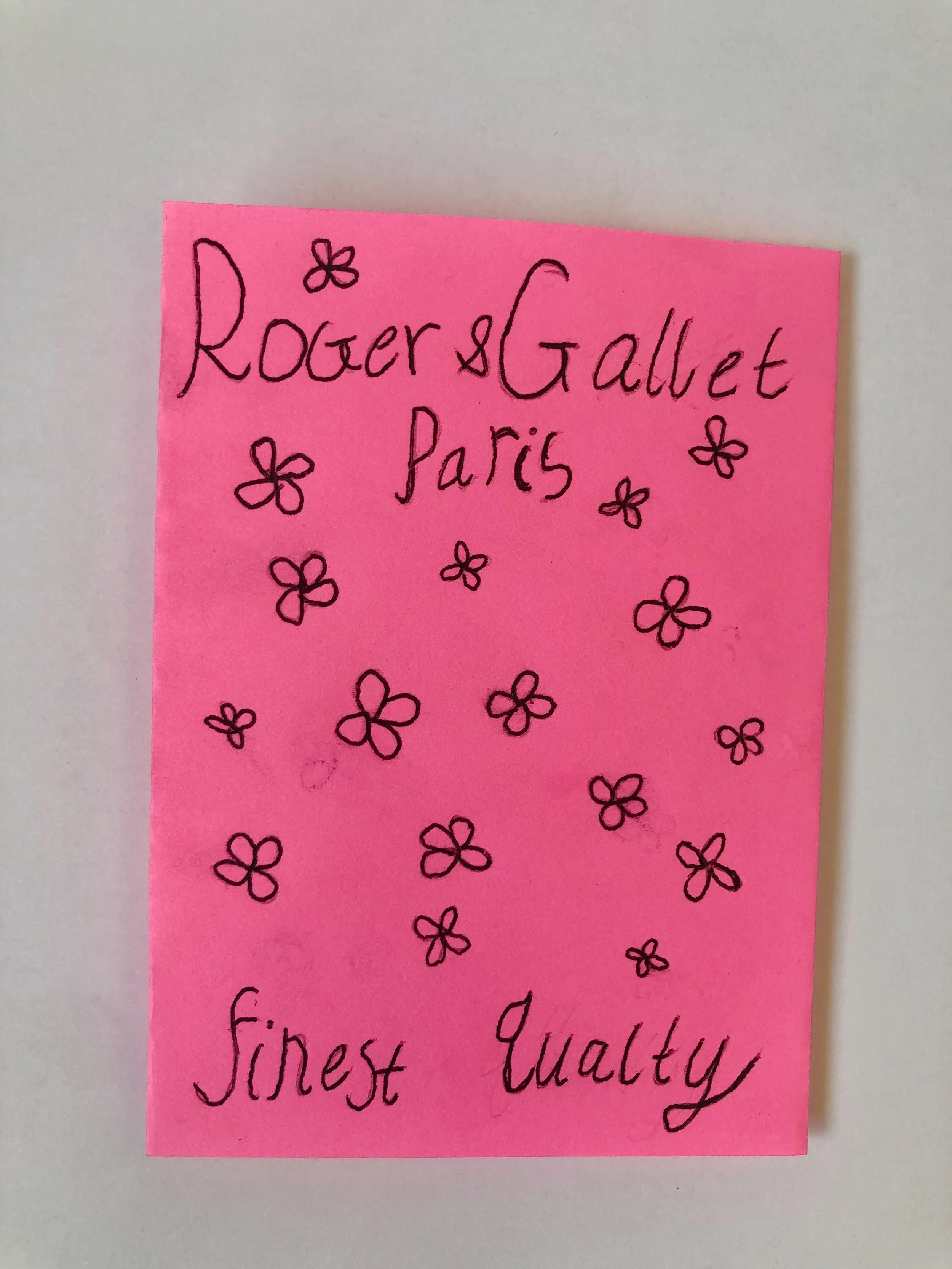 Pink sticky note with handwritten text that says 'Rogers Gallet Paris' surrounded by small flower drawings, with the words 'finest quality' at the bottom.