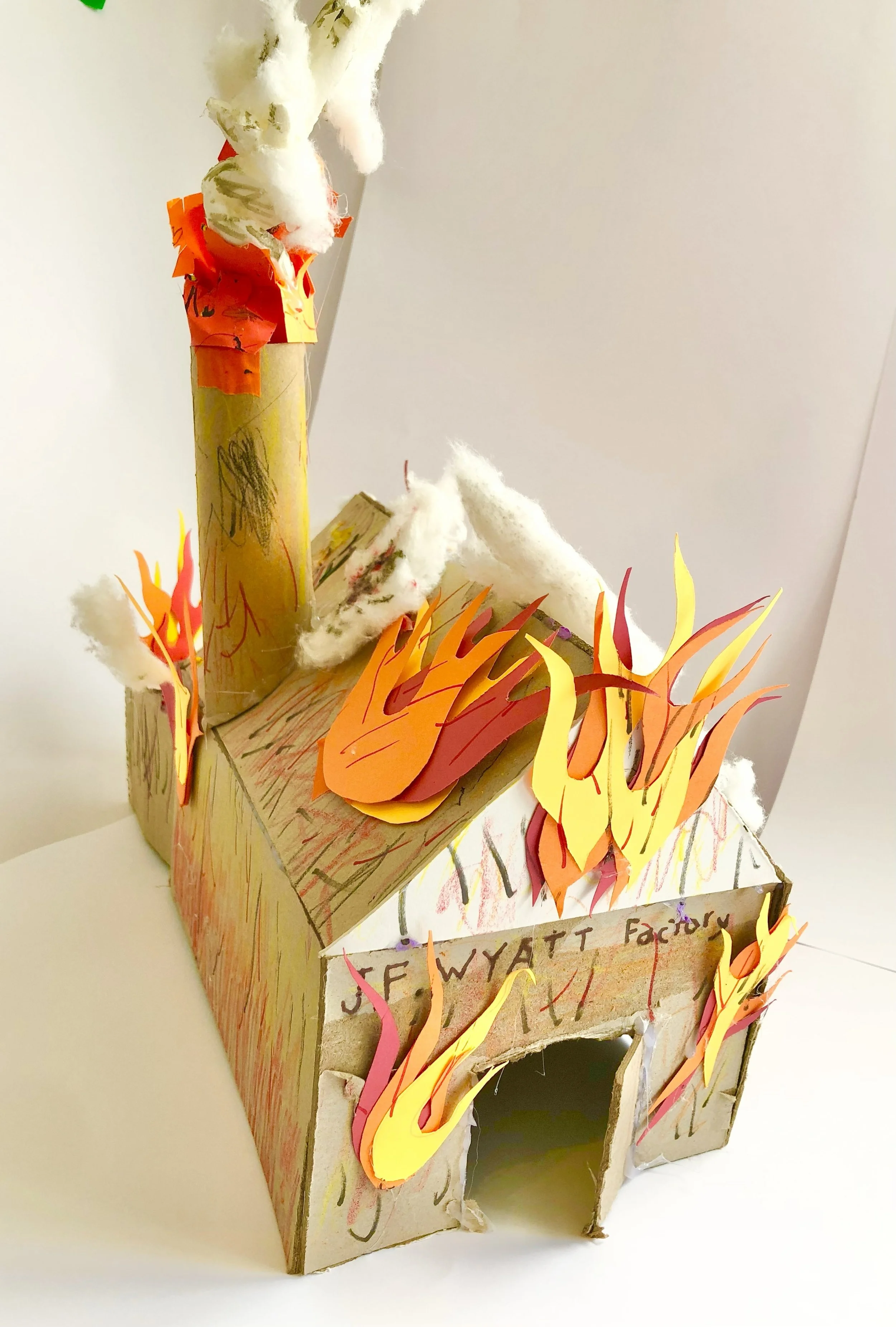 A cardboard model of a factory labeled 'J. FE WYATT Factory' with paper flames and cotton representing fire and smoke.